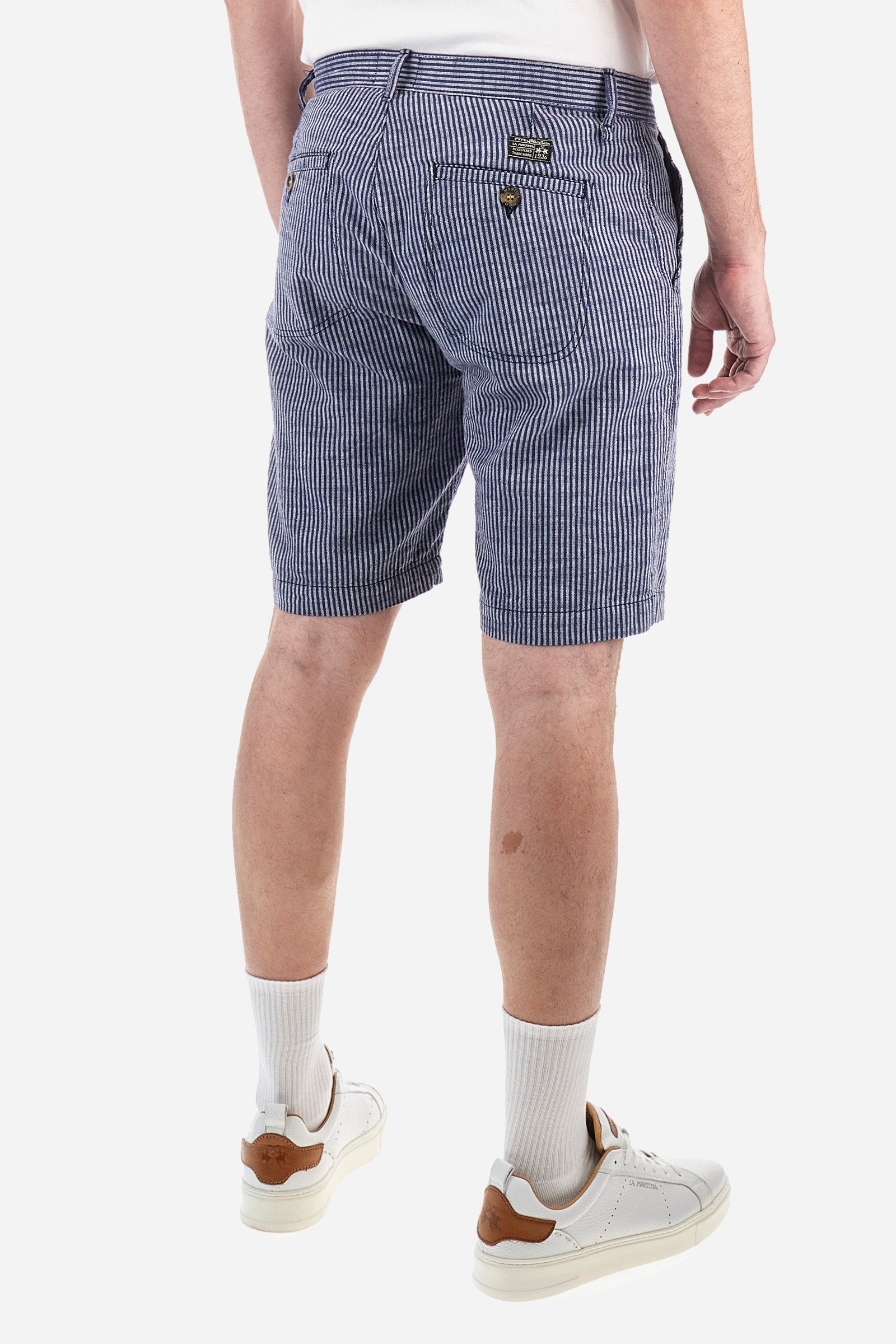 Striped men's Bermuda shorts made from luxurious cotton and linen canvas. Fastened with a zip and faux horn button. The side pockets are slanted, while the double welt back pockets are feature visible faux horn buttons and double-needle stitching around the edges. Above the right back pocket, a woven label explains the brand's quality certification. On the right hem, a graphic reading La Martina is embroidered in colourful thread. Regular fit. The model is wearing a size L. - EnsignBlue/Opt.White