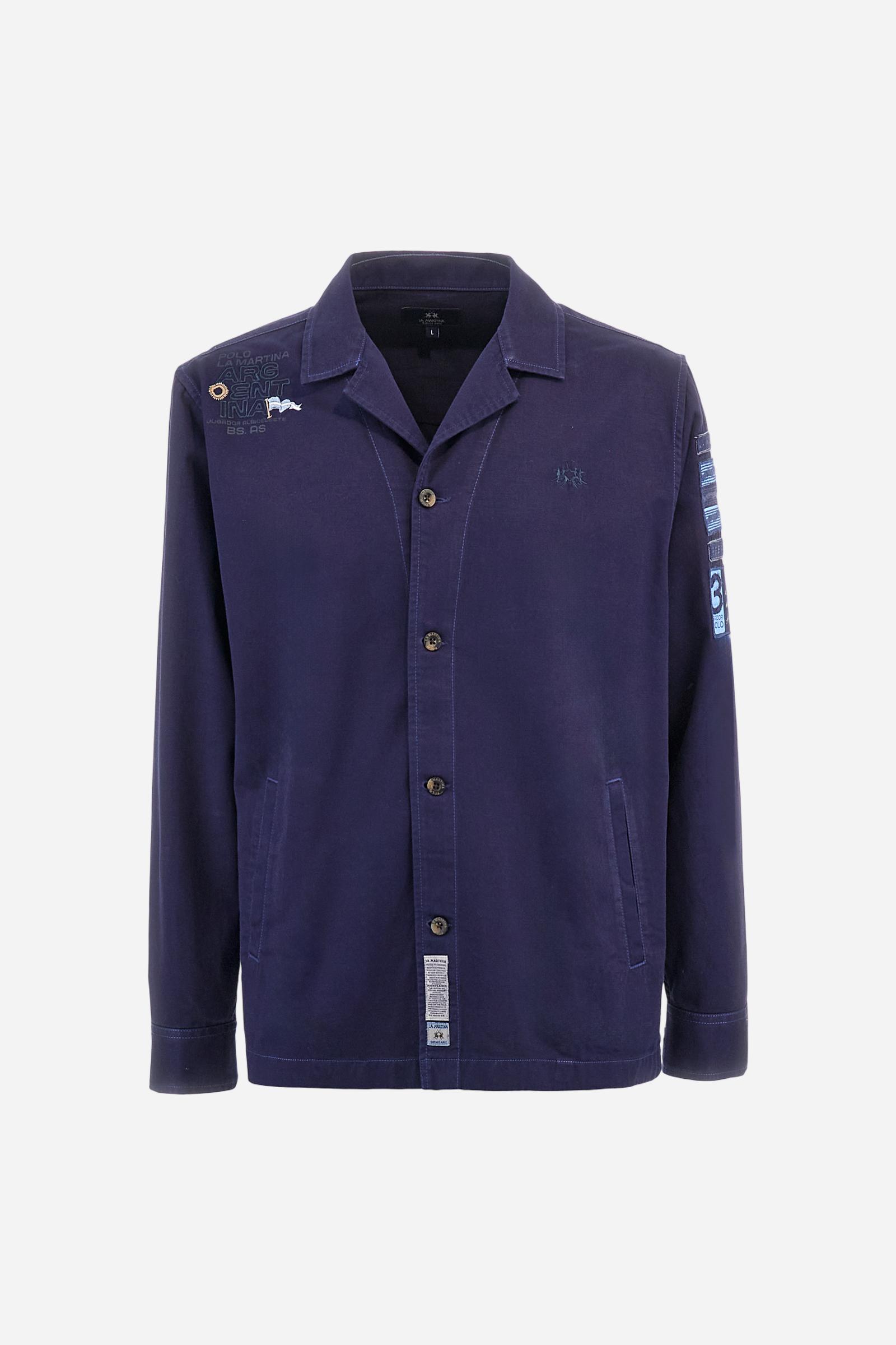 Men's single-colour long-sleeved overshirt made of 100% cotton slub twill. Bowling collar and jacket opening with inside placket, fastening with imitation horn buttons.On the shoulder and chest the embroidery is in tone with the garment, Argentina lettering embroidered on one shoulder. There are several patches applied on the left sleeve. A tone-on-tone logo is embroidered on the front. Regular fit. The model is wearing a size L. - Deep Cobalt