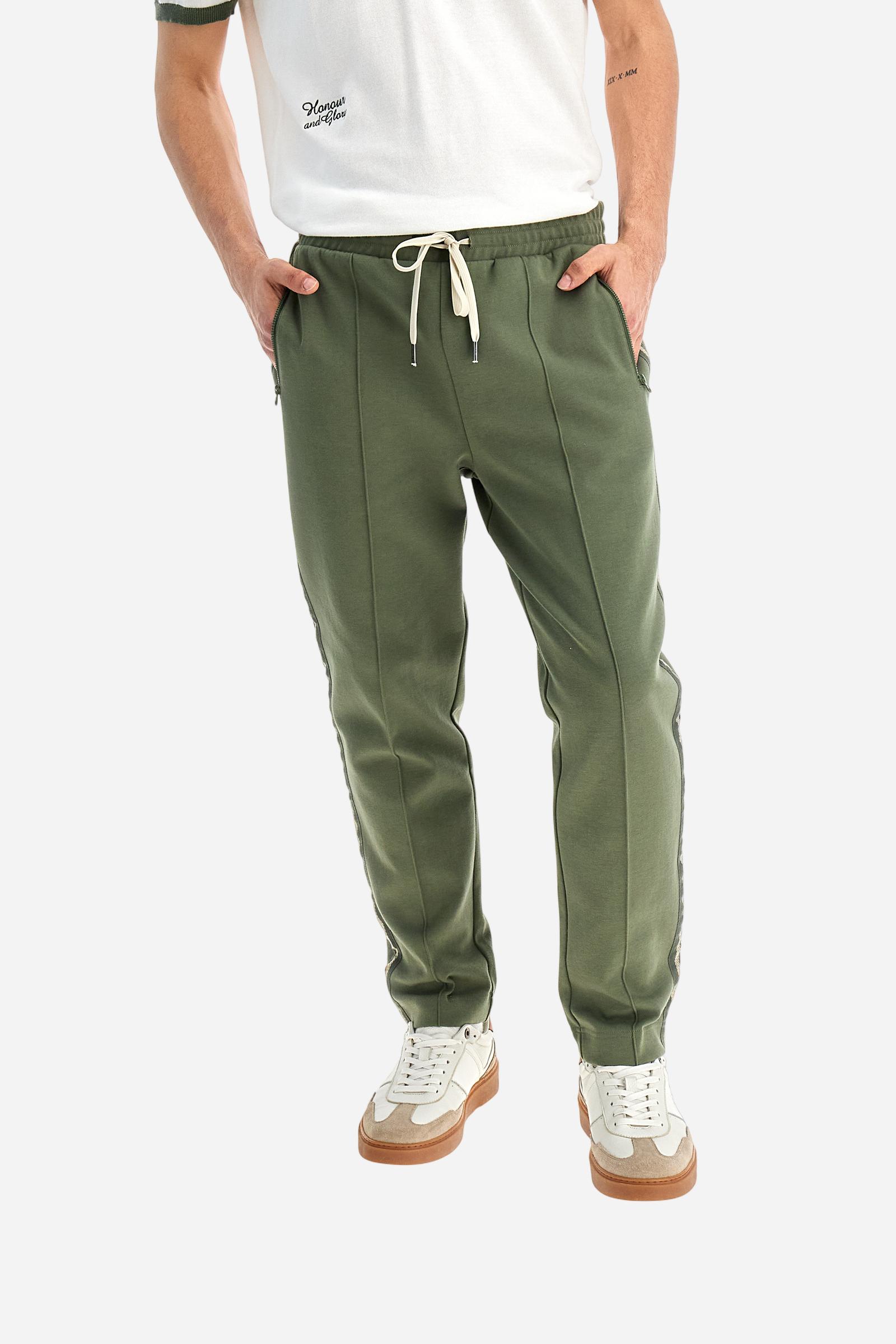 Single-colour men's jogging trousers made of lightweight cotton-blend interlock fleece. Drawstring waistband. Side pockets with matching zip fastening. On both sides, there are multicoloured striped jersey bands. The front features vertical ribbed detailing. The logo is embroidered in colour-contrasting thread on the back, under the strap, towards the right side. Regular fit. The model is wearing a size L. - Thyme