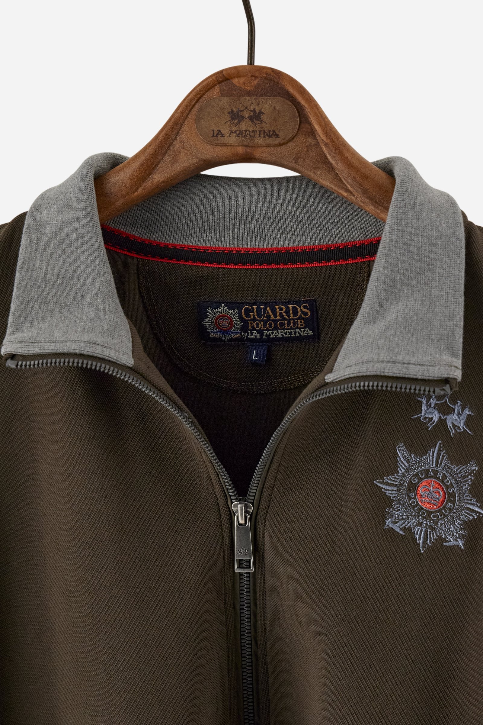 Men's long-sleeved, full-zip solid colour sweatshirt. Made of stretch cotton-blend piqué. Design with front opening fastened by a zip, high collar in two-tone ribbing. Solid colour ribbed cuffs and waistband. The small brand logo and Guards crest are embroidered in multi-coloured thread on the chest. On the right sleeve, there is another embroidery of a crest inspired by the British royal household. The regular fit silhouette is practical for everyday wear. The model is wearing a size L. - Java