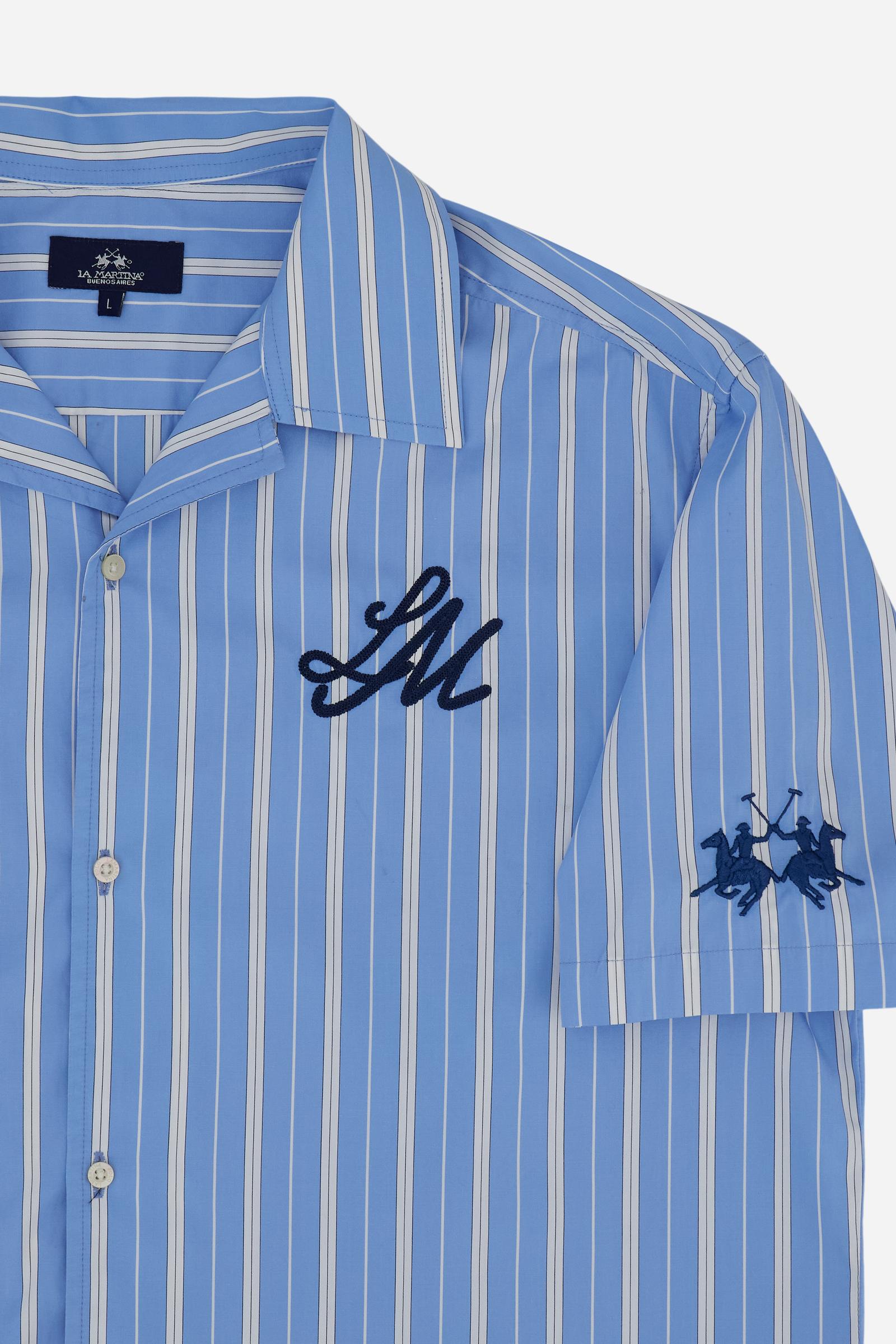 Men's short-sleeve shirt made from 100% cotton poplin with a smooth and lightweight feel. The vertical striped pattern creates a fresh summer aesthetic. The design is inspired by classic bowling shirts with an open rever collar and front button closure. The modern silhouette features dropped shoulders and a relaxed boxy cut. Sophisticated graphic details in contrasting blue include the LM initials and the embroidered brand logo on chest and sleeve, while the oversized print on the side celebrates Mykonos. T