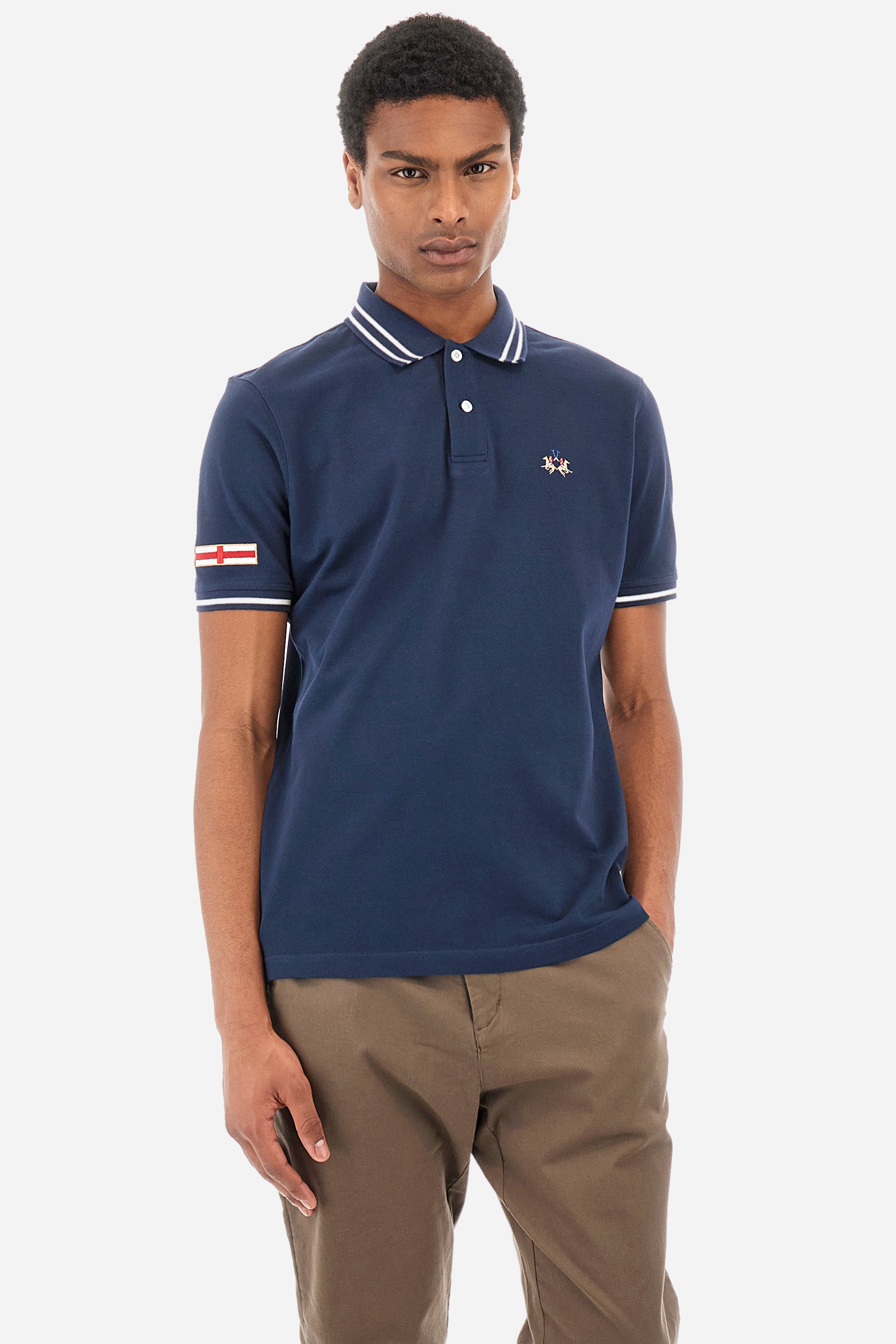 Men’s polo shirt in solid color with short sleeves in 100% cotton piquet. Two button closure. Edge and inner neck, along with the armhole all profiled with contrasting stripes. On one of the sleeves is applied a patch depicting the flag of the country to recall the capsule collection Ciudades. Small La Martina logo embroidered on the chest. The fit is regular. The model wears a size L. - Navy