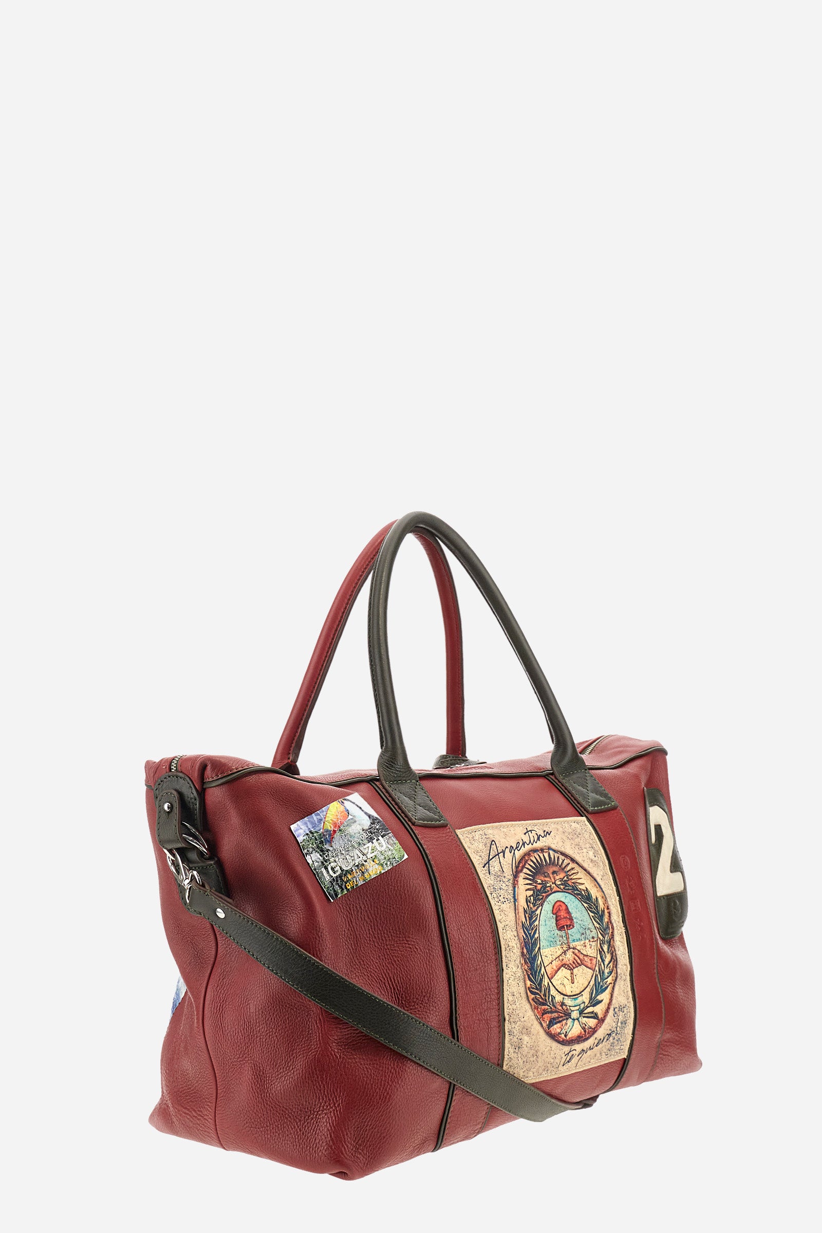 Unisex duffel bag in solid color, made of 100% leather. Iconic brand design, enriched with writings and patches. Finished with contrasting elements. Zip closure. Equipped with two handles and a removable shoulder strap. The front of the accessory features the La Martina writing and logo. The bag is adorned with stitched patches depicting landscapes and symbols related to Argentina. A leather address tag is attached to one of the handles. Dimensions (width x height x depth): 64x42x23 cm. - Barbados Cherry