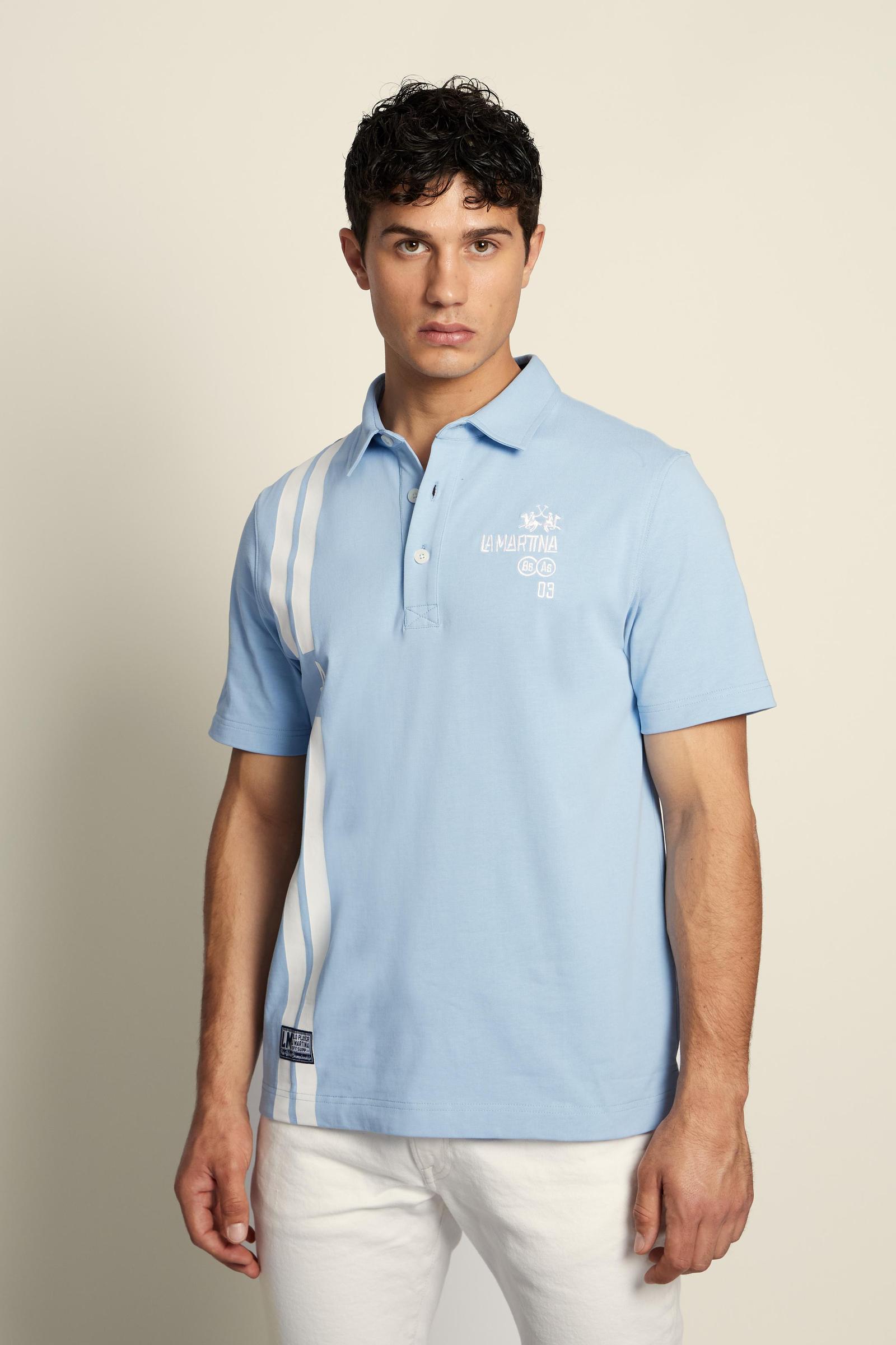 Men’s heavy cotton jersey polo with three-button placket and striped details. Celebratory maxi graphic and bold lettering. - Blue Bell