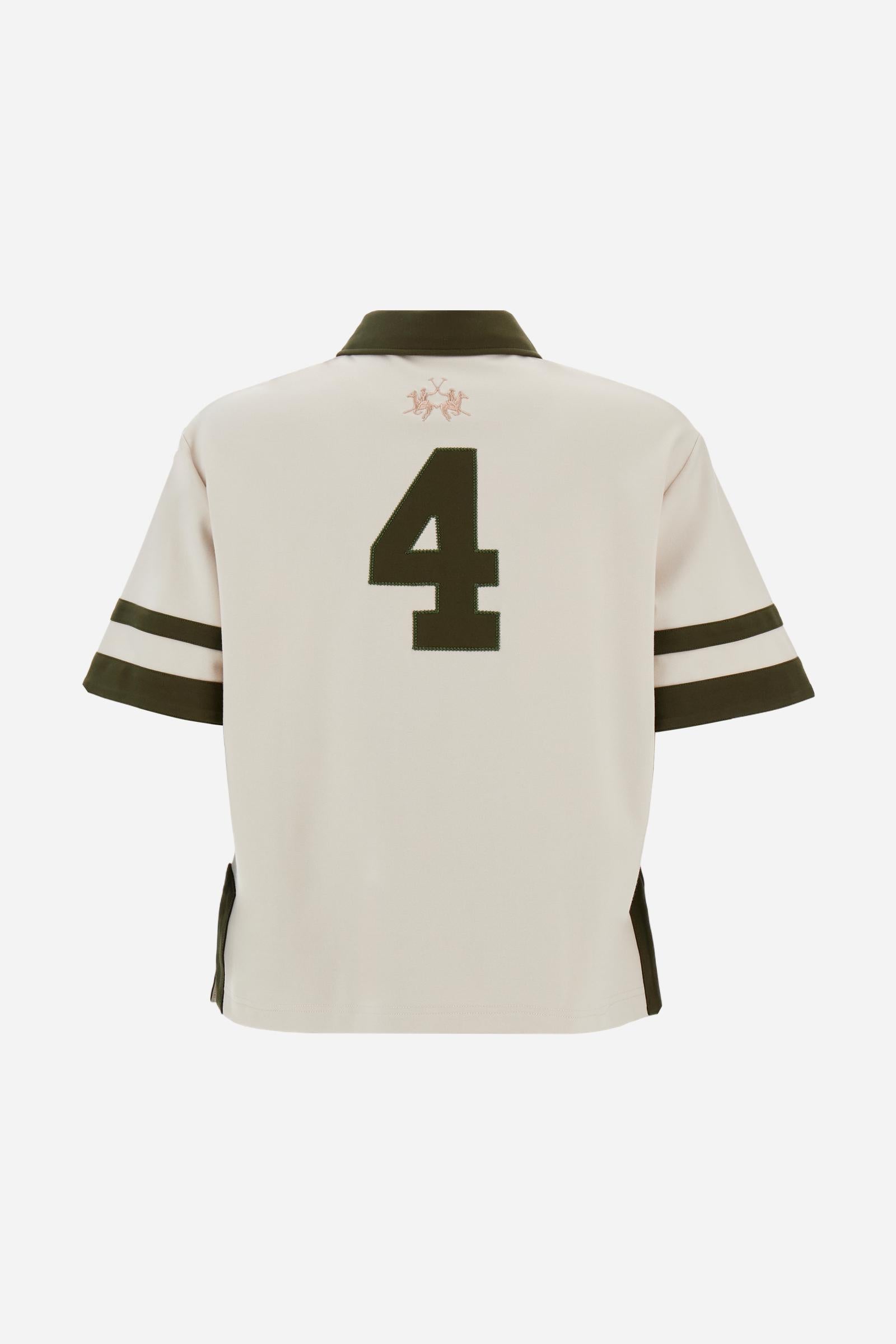 Women’s short-sleeve polo shirt in high-quality solid-colour viscose blend interlock. Classic collar with deep three-button placket, contrast fabric details on body and sleeves. Large embroidered logo on the back. Boxy, straight fit at the hips for a modern and comfortable silhouette. The model wears size L. - Creme Brulè/Kombu Gr