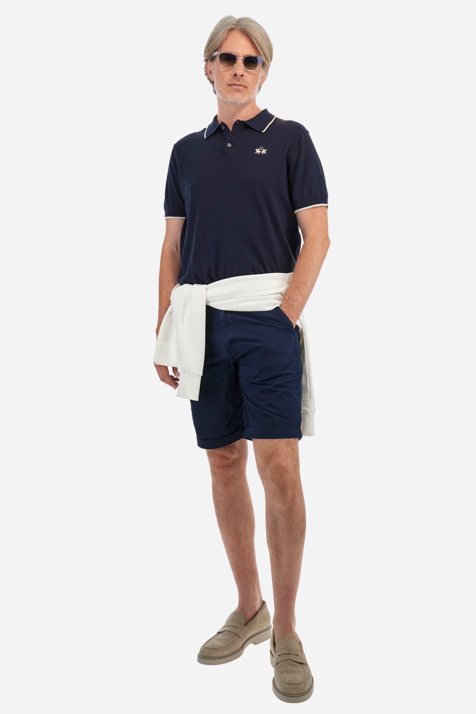 Men's plain Bermuda shorts made from cotton poplin. Fastened with a zip and faux horn button, they feature turn-ups at the hems for a touch of style. The side slant pockets are extremely practical, and the flap patch pockets on the back are fastened with faux horn buttons. Above the right pocket, a woven label explains the brand's quality certification. On the right leg, near the hem, there is an embroidered graphic with numbers and tone-on-tone lettering. Regular fit. The model is wearing a size 33. - Navy