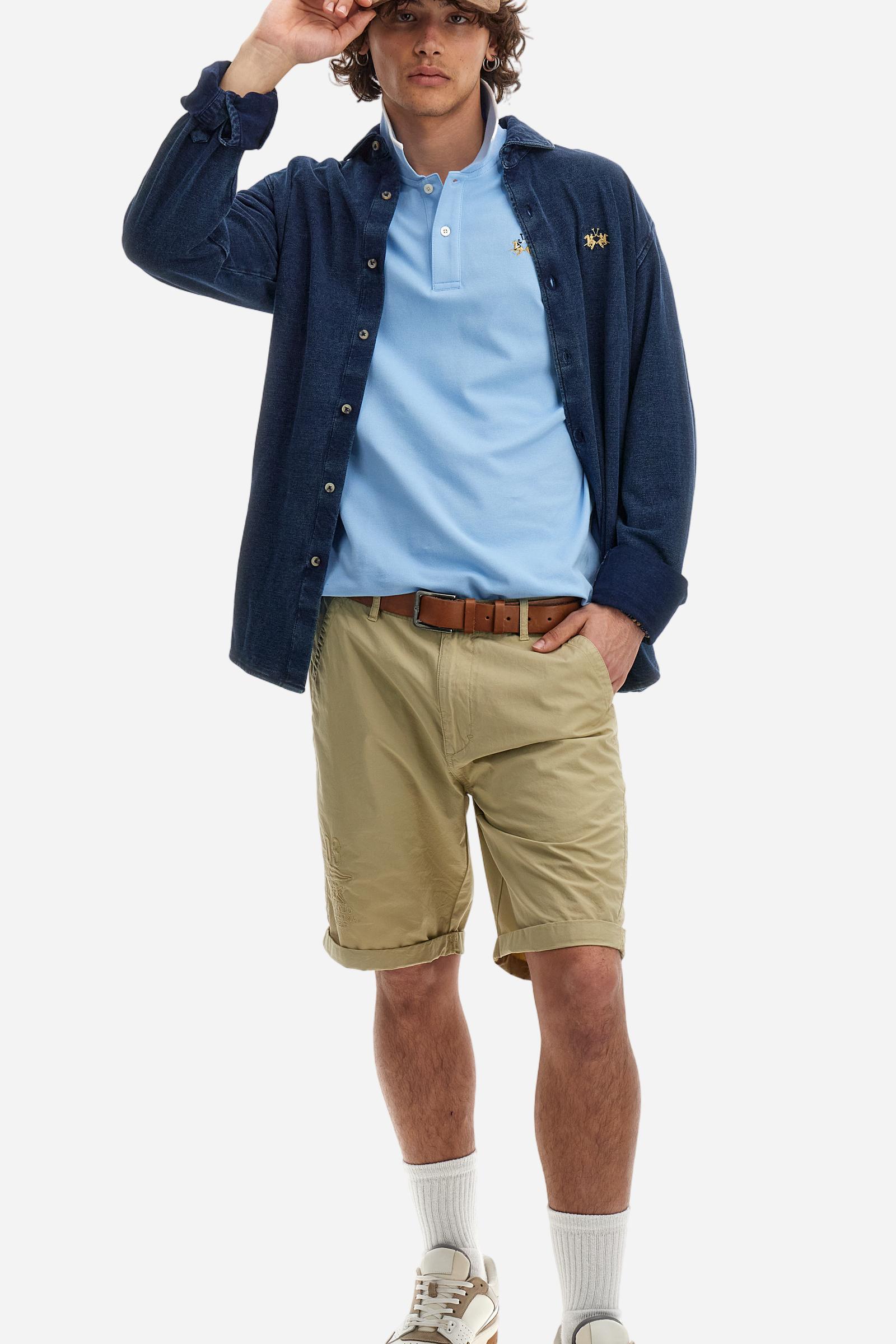 Short-sleeved, single-colour men's polo shirt made of stretch cotton piqué. Fastens with two buttons. The collar and cuffs are ribbed, and there is a colour-contrasting trim at the bottom of the collar. Inside the collar there is a grosgrain ribbon of a different shade. The logo is embroidered on the chest in a contrasting colour. The fit is slim. The model is wearing a size L. - Vista Blue