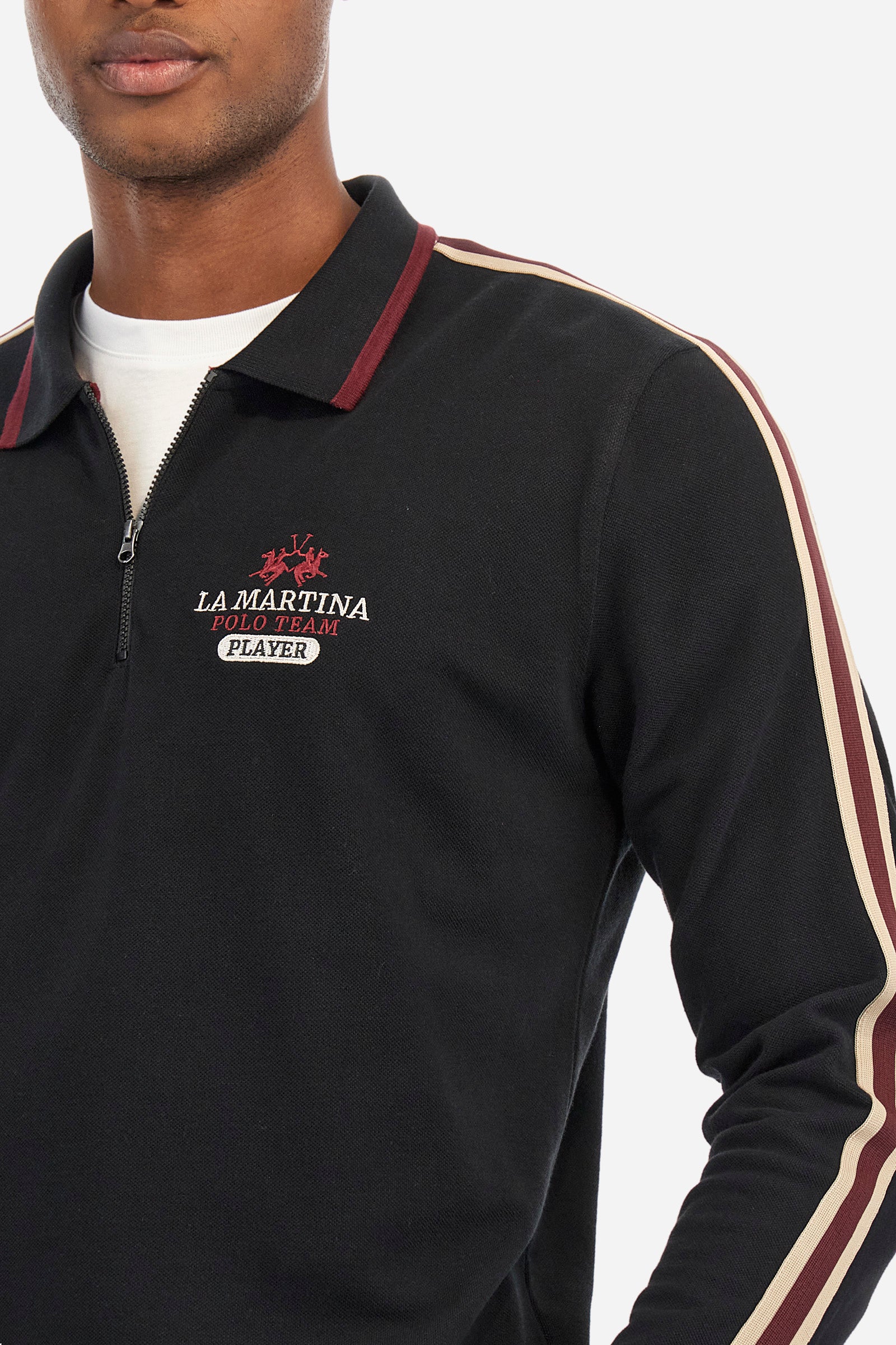 Men's plain short-sleeved polo shirt, made from 100% cotton. Half-zip fastening. Trimmed collar. The sleeves are finished with contrasting stripes. The symbols and lettering associated with the Harvard line are appliquéd on the back. The front is embroidered with the logo and La Martina lettering. Regular fit. The model is wearing a size L. - Black