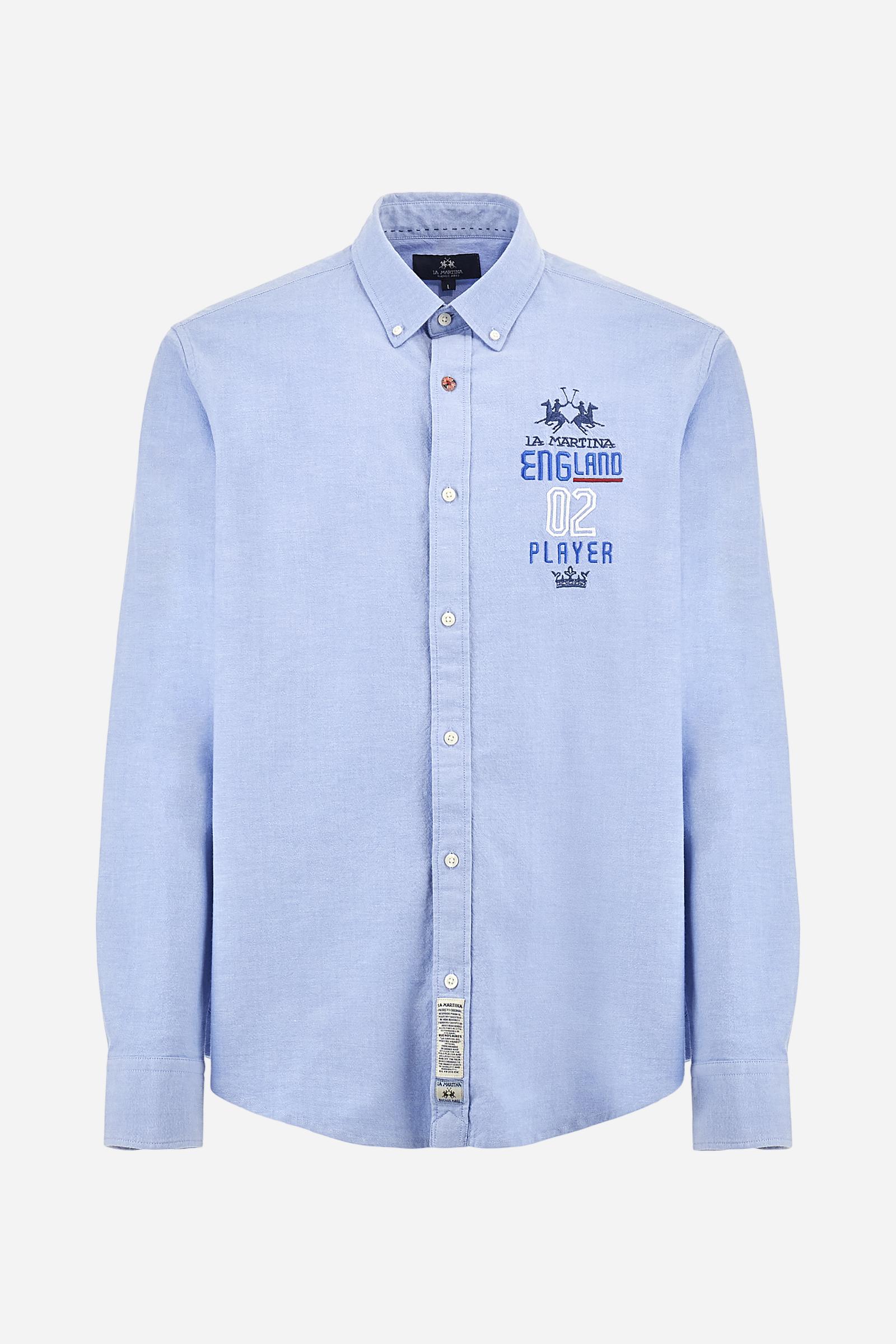 Men's long-sleeved plain shirt made from 100% Oxford cotton. The button-down collar is finished with a second button printed with the English flag. The multicoloured embroidery on the chest, over the heart, includes lettering, numbers and the logo, which add a distinctive touch. Regular fit. The model is wearing a size L. - Cornflower blue