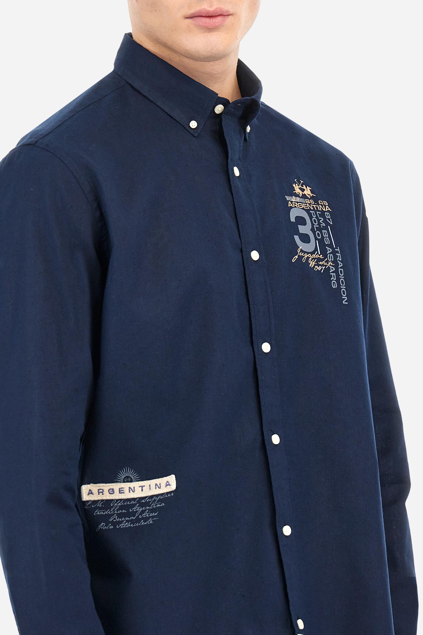 Men's plain long-sleeved shirt made from cotton and linen canvas. Featuring a button-down collar and sleeve openings embellished with contrasting fabric details. The graphic on the chest, over the heart, is created using a combination of embroidery and printing techniques to add a distinctive touch. On the side, at the front, there is a ribbon embroidered with the word Argentina, topped with a print. Regular fit. The model is wearing a size L. - Navy