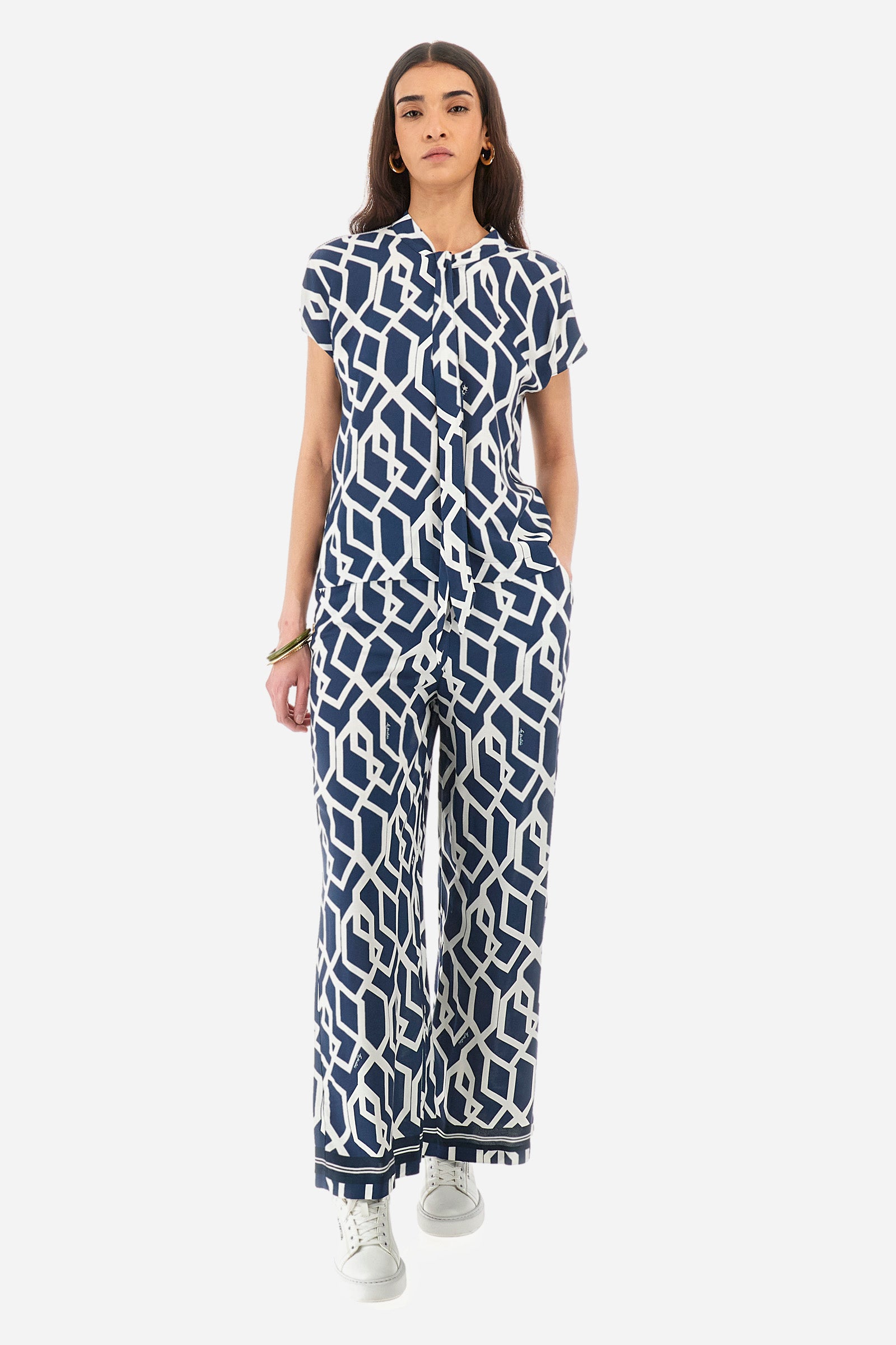 Women's short-sleeved blouse with a geometric print, made of synthetic fabric. A shawl collar. A small logo is present on a metal plate applied to the front and printed on the collar tie. The fit is regular. The model wears a size 2. - Orion blue/Off white