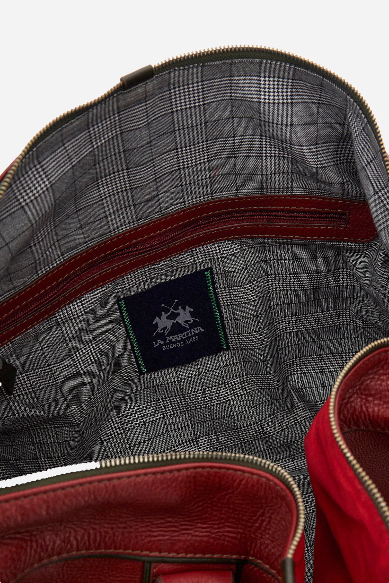 Unisex duffel bag in solid color, made of 100% leather. Iconic brand design, enriched with writings and patches. Finished with contrasting elements. Zip closure. Equipped with two handles and a removable shoulder strap. The front of the accessory features the La Martina writing and logo. The bag is adorned with stitched patches depicting landscapes and symbols related to Argentina. A leather address tag is attached to one of the handles. Dimensions (width x height x depth): 64x42x23 cm. - Barbados Cherry