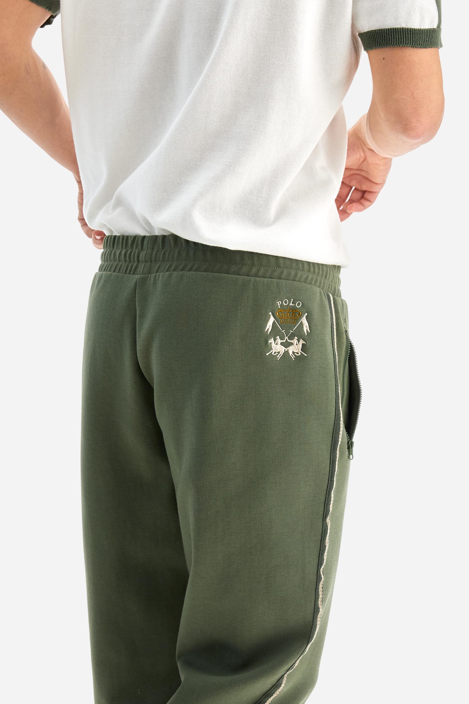 Single-colour men's jogging trousers made of lightweight cotton-blend interlock fleece. Drawstring waistband. Side pockets with matching zip fastening. On both sides, there are multicoloured striped jersey bands. The front features vertical ribbed detailing. The logo is embroidered in colour-contrasting thread on the back, under the strap, towards the right side. Regular fit. The model is wearing a size L. - Thyme