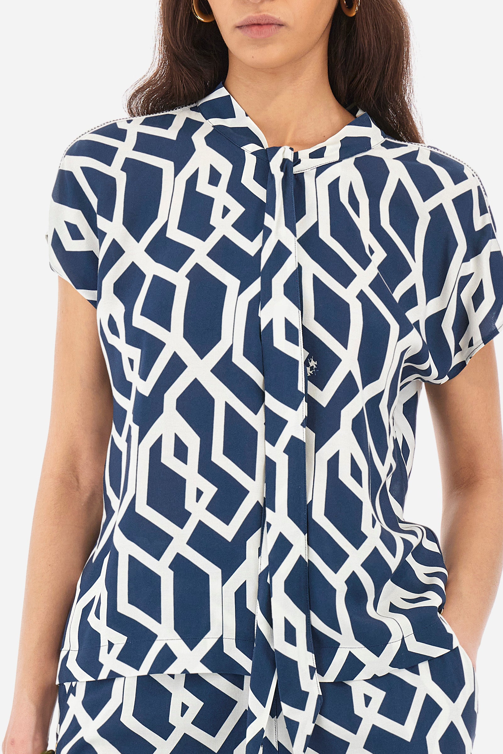 Women's short-sleeved blouse with a geometric print, made of synthetic fabric. A shawl collar. A small logo is present on a metal plate applied to the front and printed on the collar tie. The fit is regular. The model wears a size 2. - Orion blue/Off white