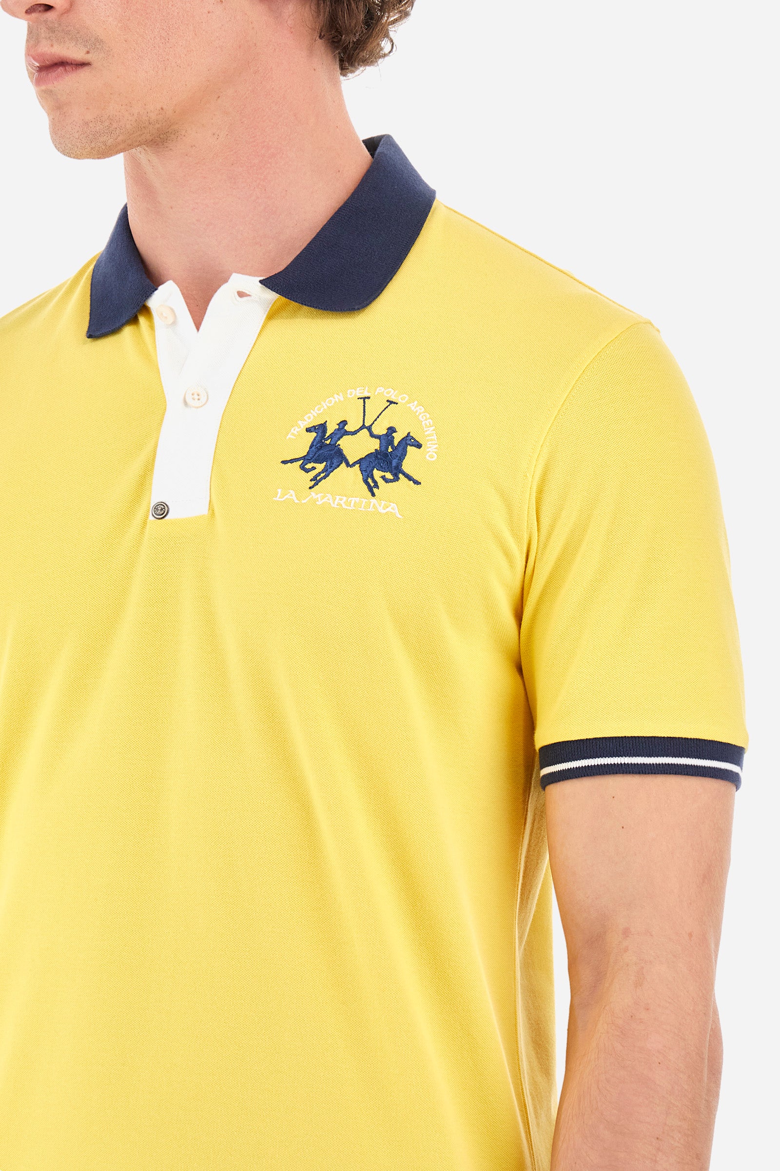 Men's single-colour short-sleeved polo in elasticated cotton. Fastens with two contrasting buttons. Ribbed collar and armholes in different shades. The "La Martina" lettering can be found under the collar. A large logo is embroidered on the chest. The fit is slim. The model wears a size L. - Aspen Gold
