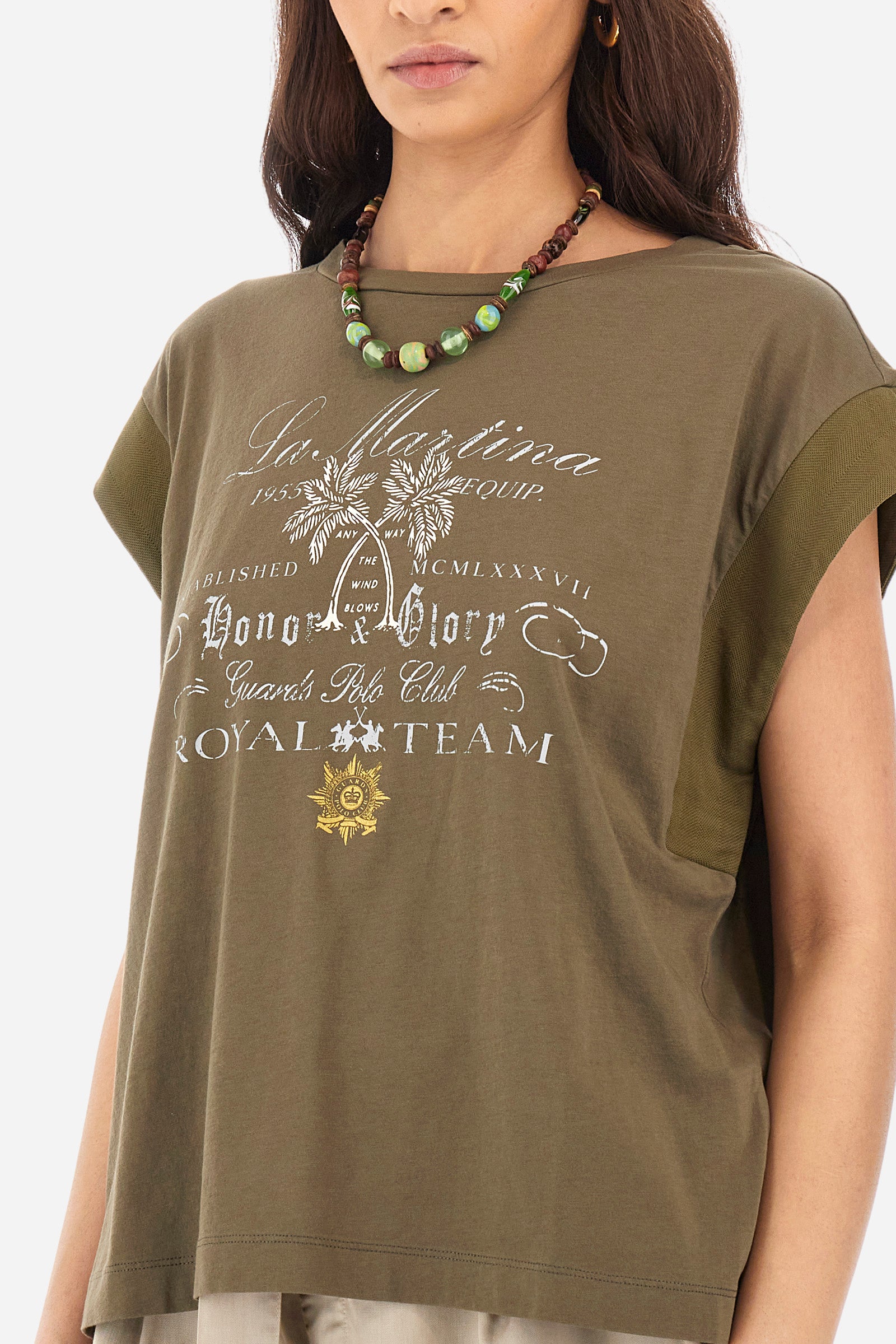 Women’s crew neck short-sleeved t-shirt in solid color, made of 100% cotton jersey. On the front we find an embroidered mini logo La Martina together with the symbol of the capsule collection Guards, in contrasting tone, which are accompanied by palm prints. Two mini side slits. The fit is regular. The model wears a size 2. - Military Olive
