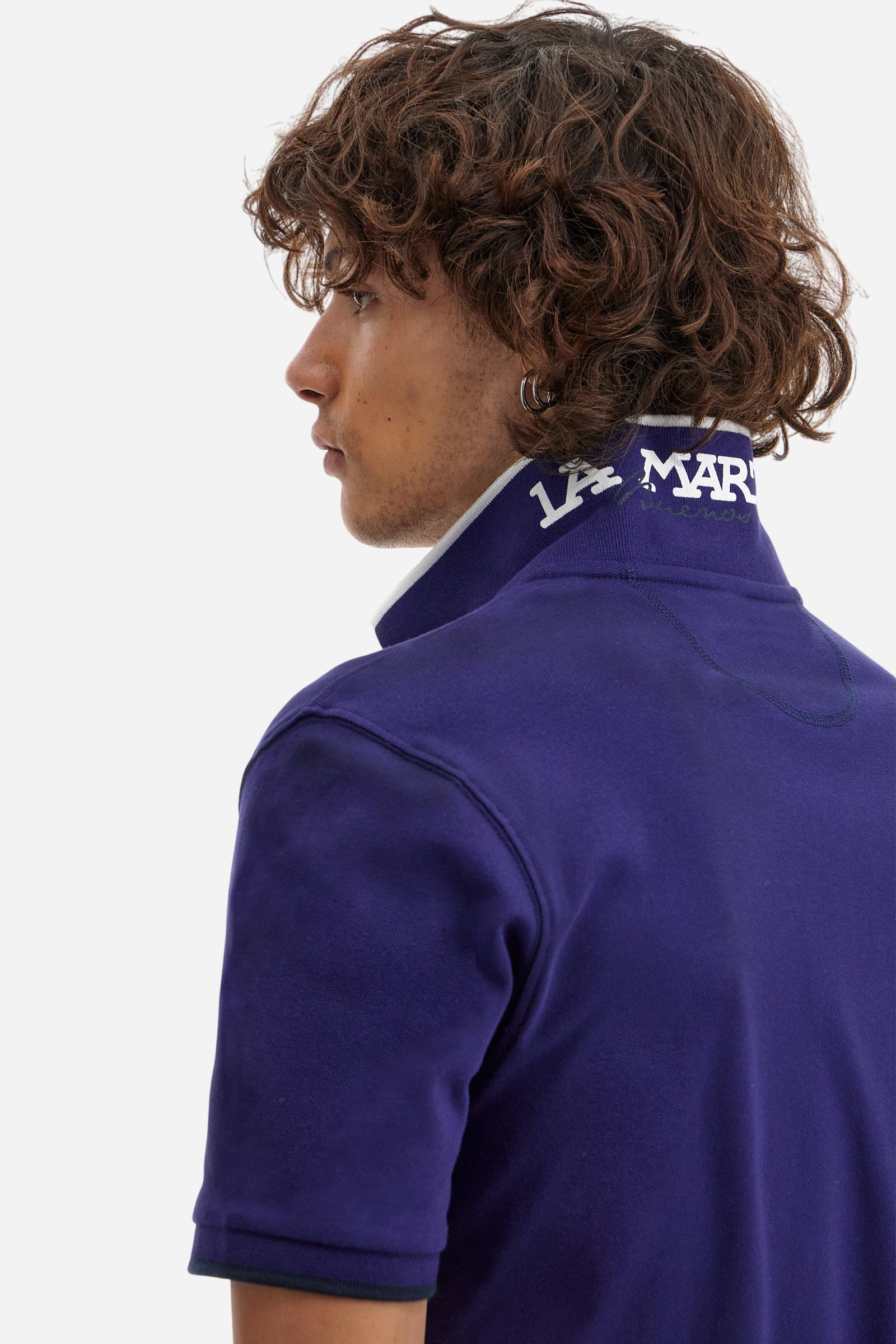 Short-sleeved, single-colour men's polo shirt made of stretch cotton piqué. Fastens with two buttons. The collar and cuffs are ribbed, and there is a colour-contrasting trim at the bottom of the collar. Inside the collar there is a grosgrain ribbon of a different shade. The logo is embroidered on the chest in a contrasting colour. The fit is slim. The model is wearing a size L. - Deep Cobalt