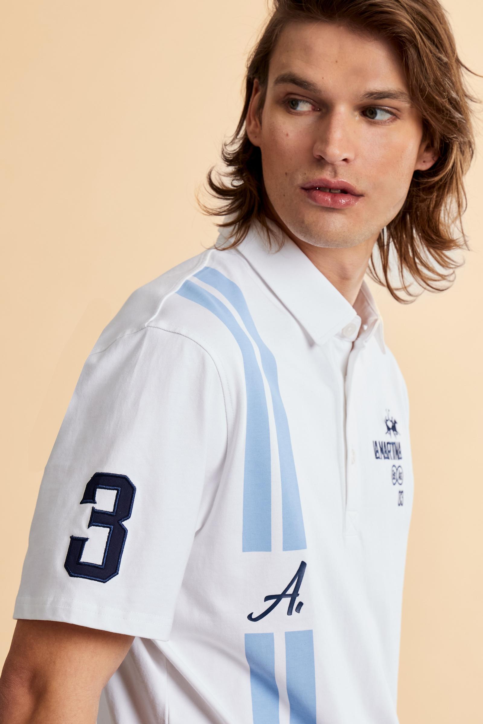 Men’s heavy cotton jersey polo with three-button placket and striped details. Celebratory maxi graphic and bold lettering. - Optic White