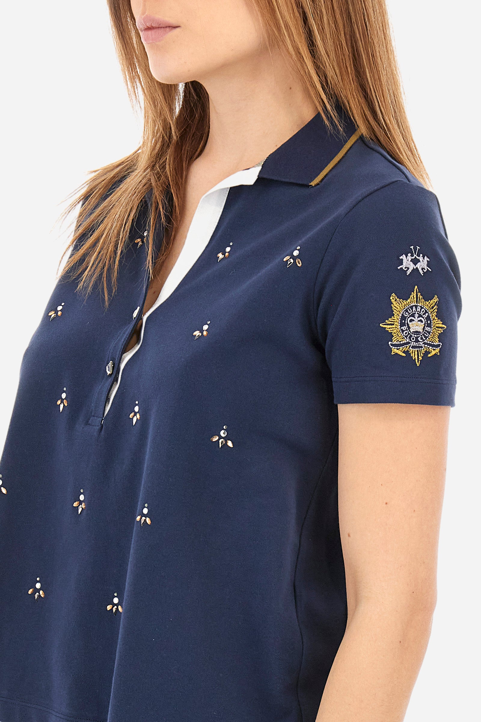 Women’s polo with short sleeves in solid color from the Guards line. Made of stretch cotton. V-neck and 2-button jewel closure. Ribbed collar. Side slits. Rhinestones of various shapes, sizes and colors were applied to the front. The logo and the characteristic symbol of the line are embroidered on a sleeve. The fit is regular. The model wears a size 2 . - Navy
