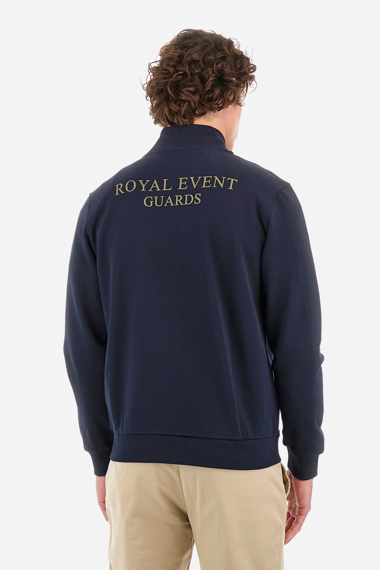 Men’s solid color long sleeve sweatshirt with full zip closure. Made of 100% cotton. High neck with drawstring, ribbed hem and cuffs. Double front pocket with button closure. Writing and large symbol on the chest identify the capsule collection. The fit is regular. The model wears a size L. - Navy