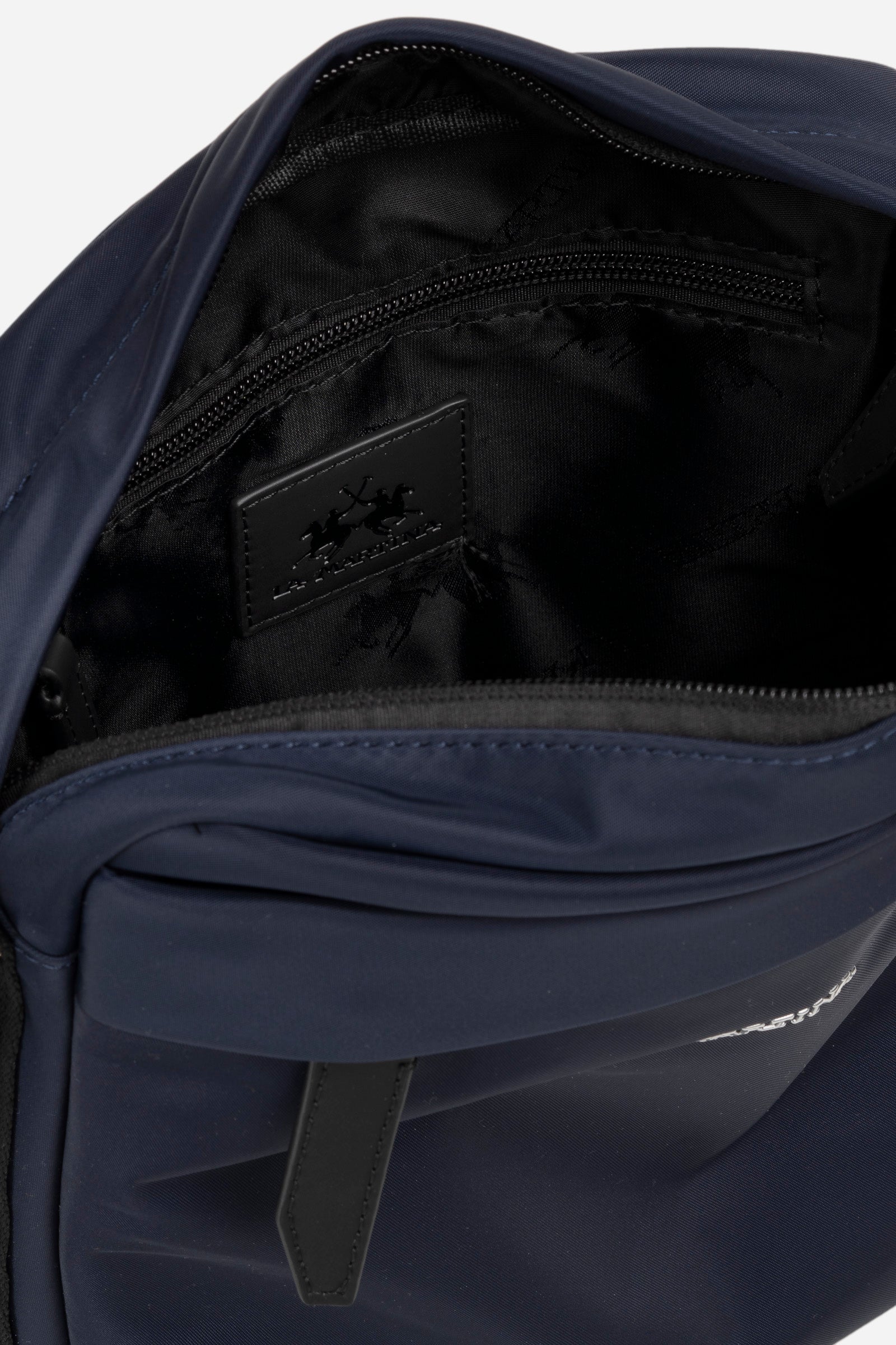 Single-colour men's crossbody bag in nylon with polyurethane details With zip fastening. There are two additional external pockets, one with a zip fastening and one with a magnetic button. Adjustable fabric shoulder strap. On the back is another pocket with a pneumatic closure. The inside features two pockets: one open pocket and one with a zip. The lettering "La Martina" is positioned on the front in metal. Dimensions (length x height x width) 21 x 26 x 7 cm. - Navy