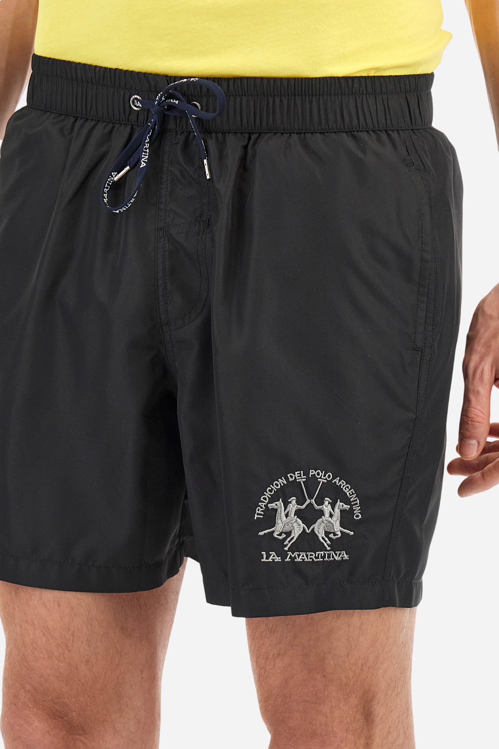 Plain men's swimming shorts made of nylon. Elastic waistband with a personalised drawstring for waist adjustment. On the inside of the shorts is an elasticated mesh brief. Double side pocket on the hips and patch pocket with flap on the back, on the right side only. The large logo is embroidered in a contrasting colour thread on the bottom of the left leg on the front. Regular fit. The model is wearing a size L. - Black