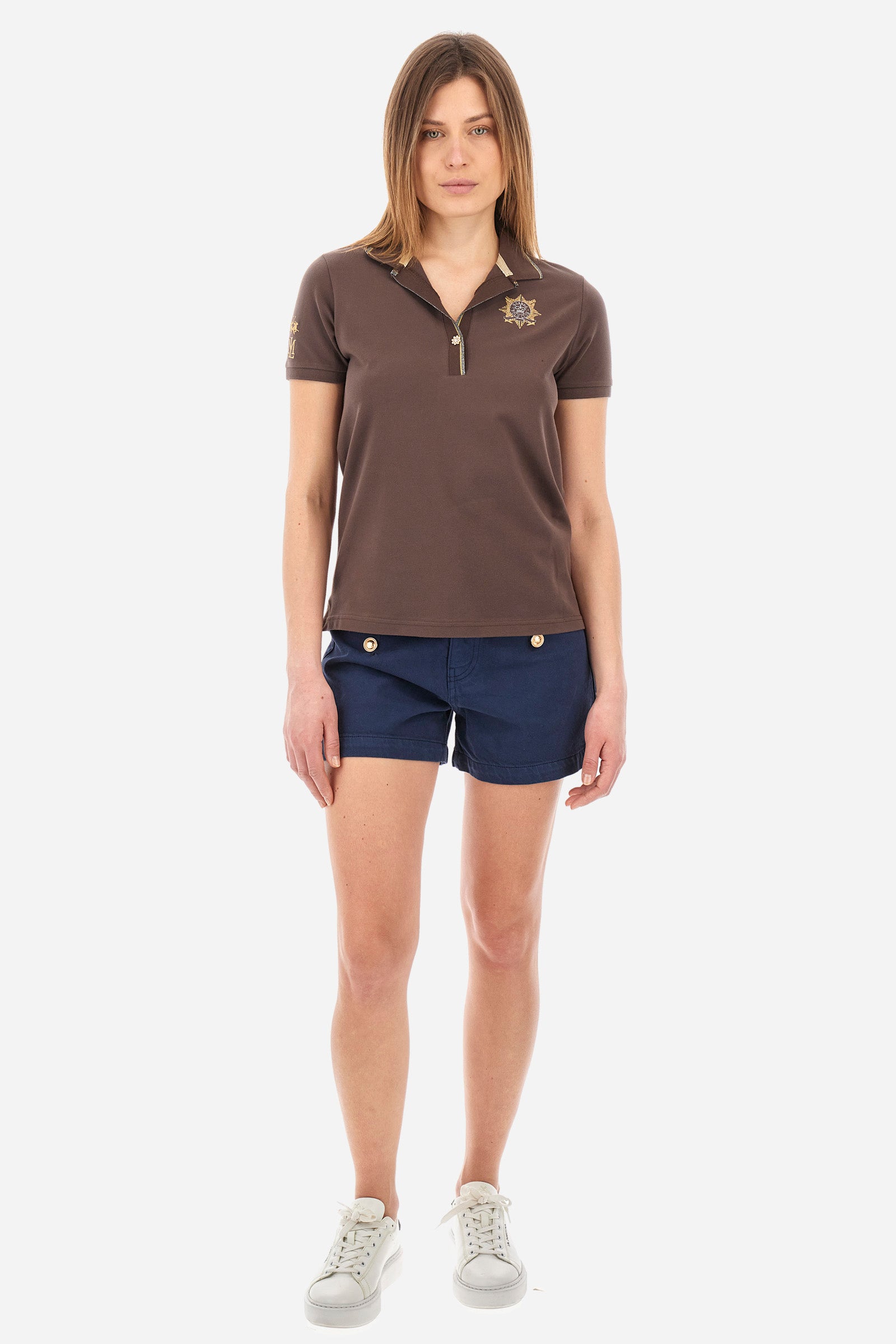 Women’s polo with short sleeves in solid color. Made of stretch cotton. V-neck and jewel button closure. Ribbed crew neck and armhole, both profiled by a lamé strip. The under collar embellished with a different color print along with mini logo and symbol on the chest and sleeve are characteristic of the capsule Guards. The fit is regular. The model wears a size 2. - French Roast