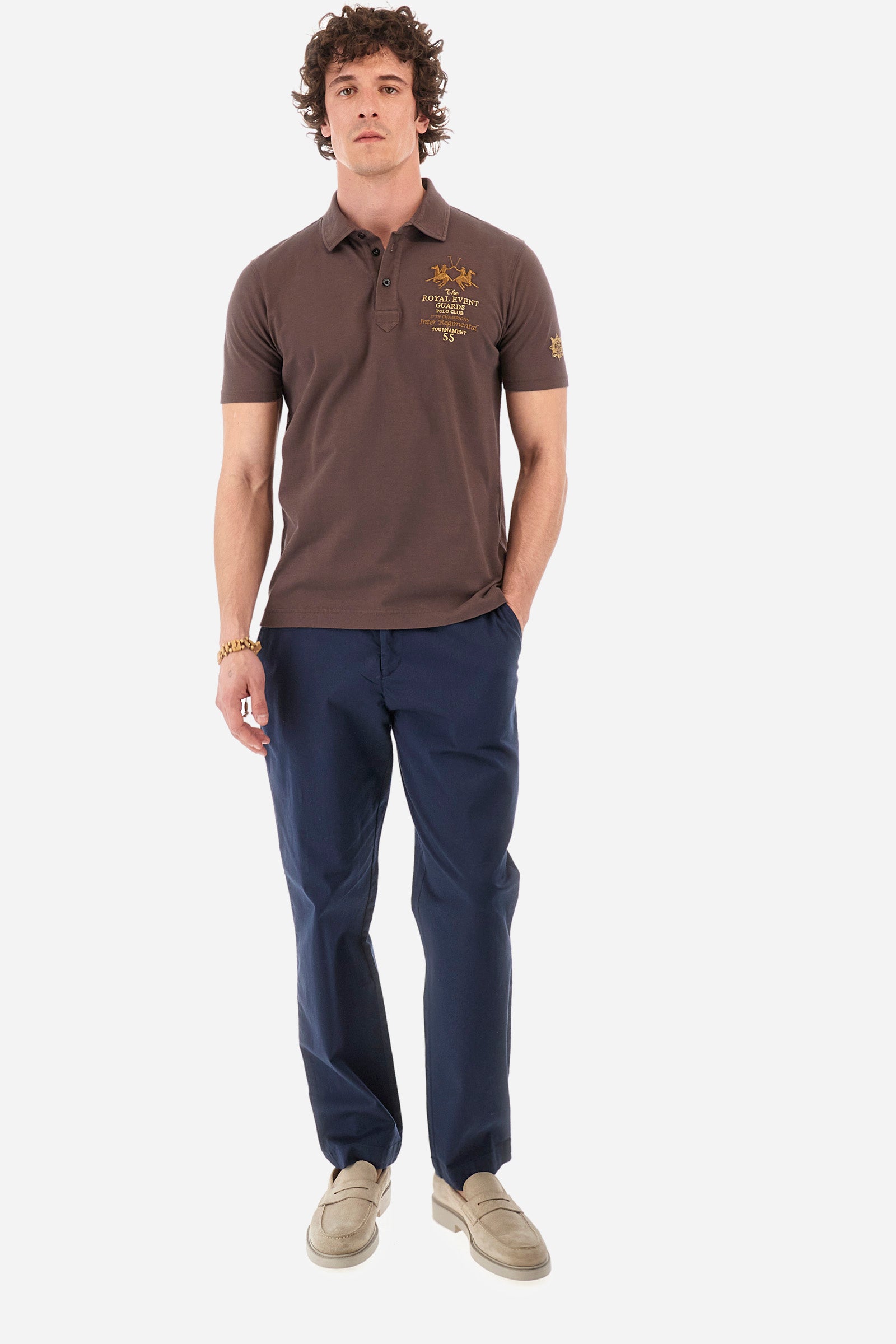 Men's short-sleeved single-colour polo shirt in elasticated cotton. Two-button fastening. Pointed collar. On the front we find copper-coloured lettering and a large logo. On one of the sleeves there is a symbol representing the Guards line. The fit is regular. The model wears a size L. - French Roast