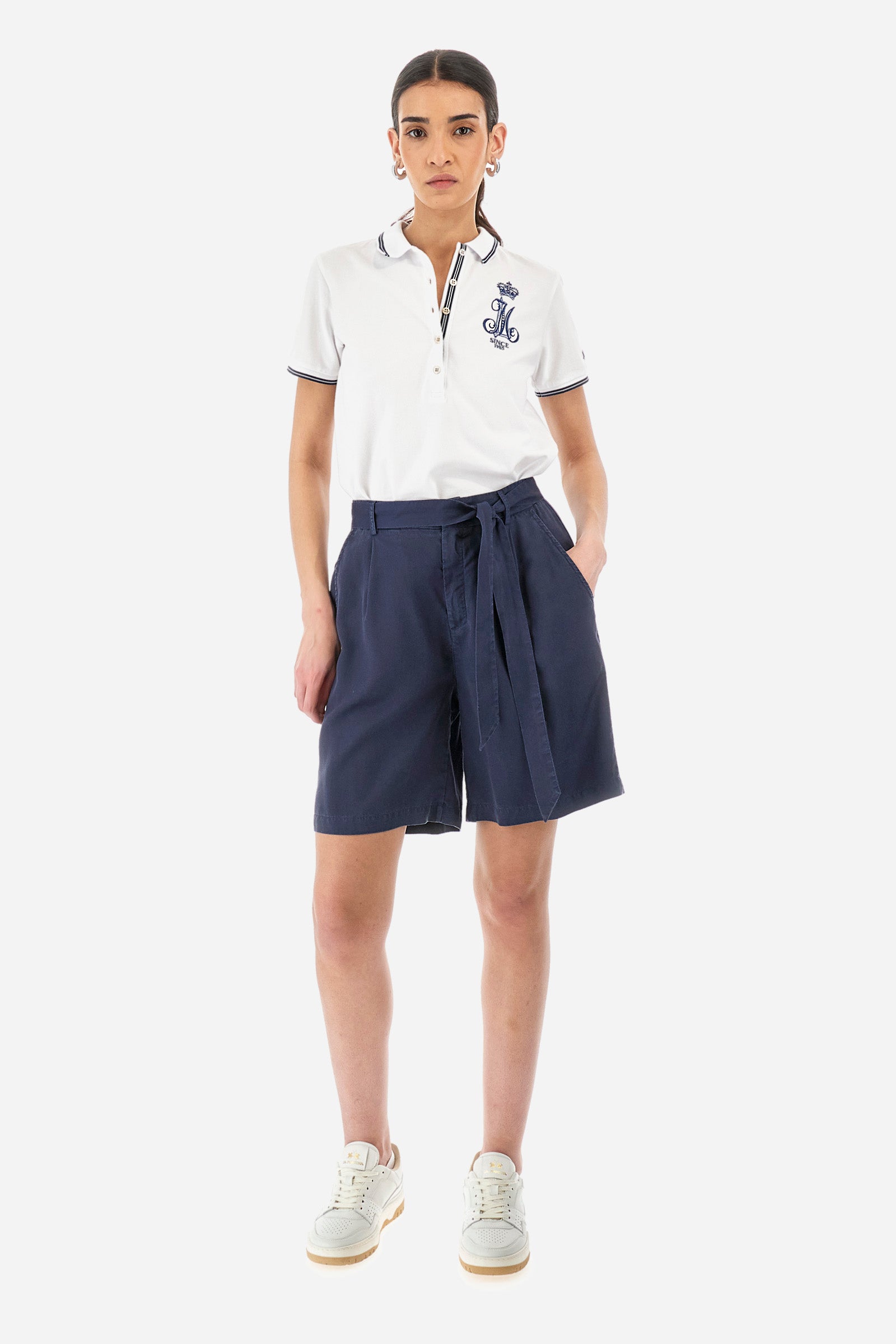 Women’s polo with short sleeves in solid color, made of stretch cotton. 5-button closure, ribbed collar and crew sleeves, where contrasting stripes are sewn. Side slits. On the front are embroideries with symbols and initials of the brand, recalling the capsule collection Polo Club Grand Hotel. The logo is embroidered on a contrasting sleeve. The fit is regular. The model wears a size 2. - Optic White