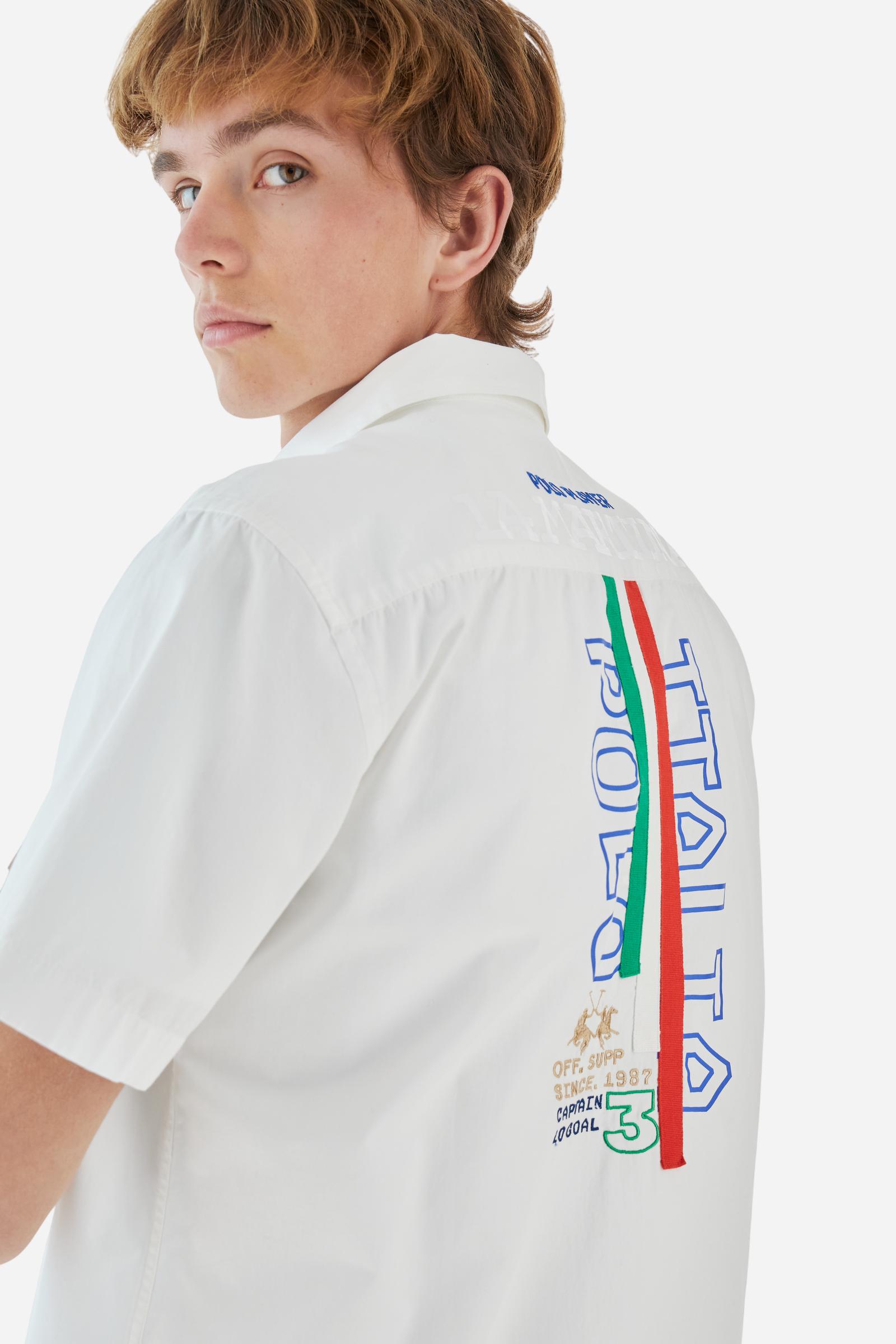Men's plain short-sleeved shirt made from cotton poplin. Spread collar and straight hem. The embroidered logo on the chest, over the heart, is designed in the colours of the Italian flag. On the back, the combination of printing and embroidery techniques – depicting lettering, numbers and logos – are enriched with 3 ribbons in the colours of the Italian flag, appliquéd vertically. Regular fit. The model is wearing a size L. - Optic White