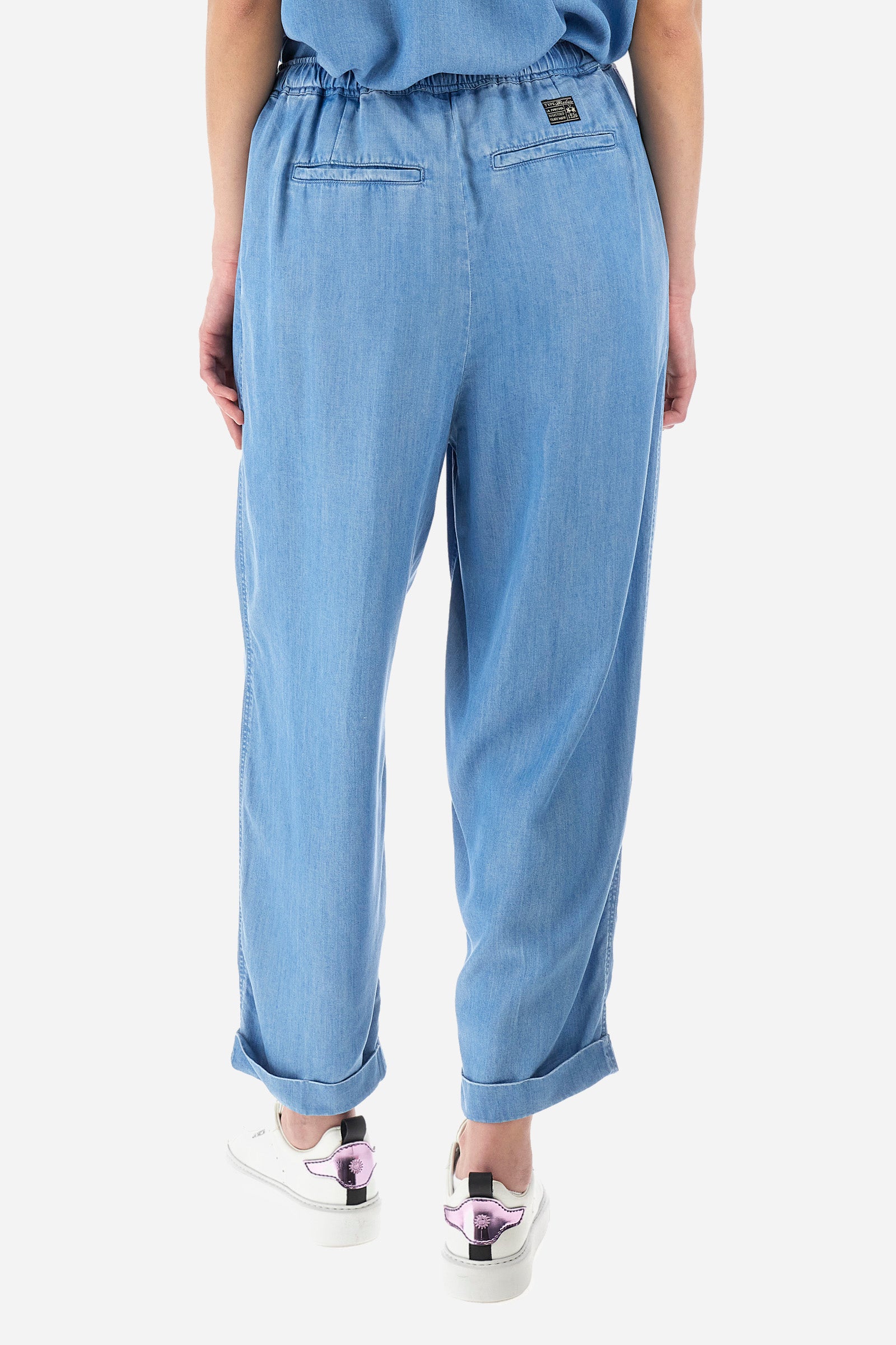Women’s trousers in solid color, made of ecological lyocell denim fabric. Drawstring waist and laces to adjust the closure comfortably. Two front and two back pockets, all flush. The logo is present on a patch sewn on the back and on a metal plate on the front. The fit is regular. The model wears a size 2. - Medium Indigo Denim