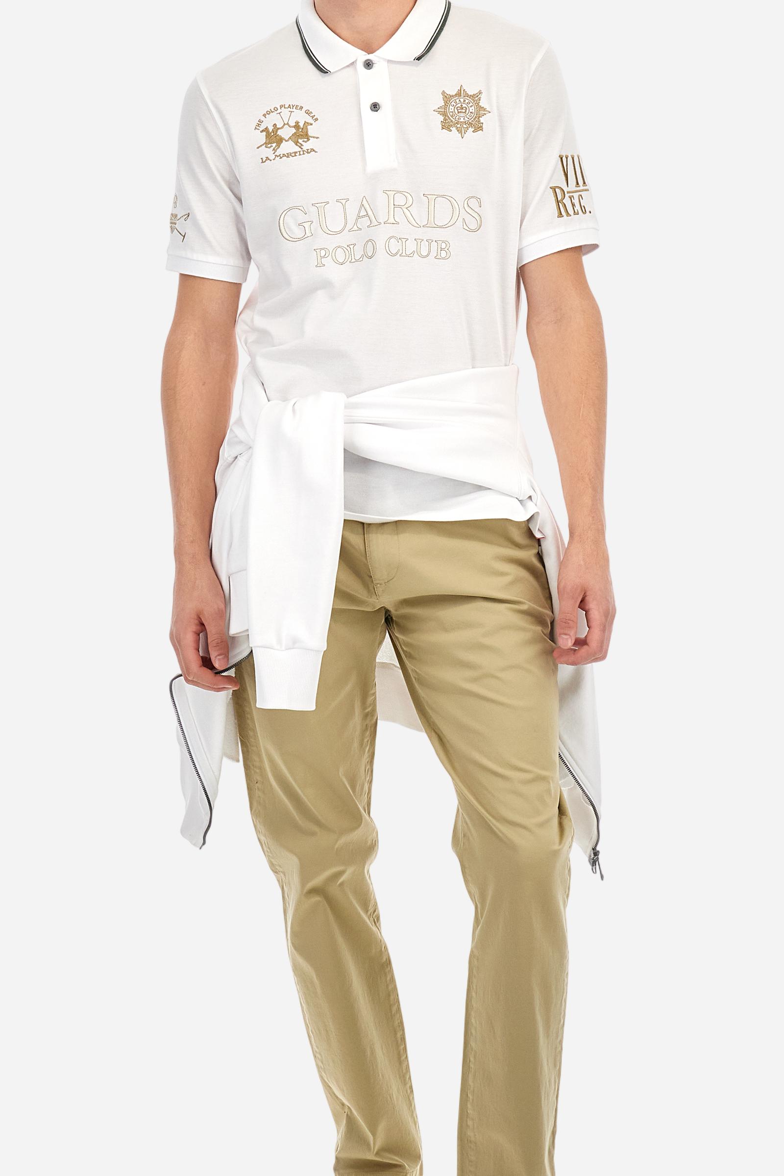 Men's short-sleeved Guards polo shirt in a single colour, made of cotton piqué. Fastens with two buttons. The collar is ribbed with striped trim in a contrasting colour. The graphics on the chest and sleeves are all made using the embroidery technique. The central lettering on the chest is a 3D embroidery in the same colour as the base fabric. The large colour-contrasting logo is embroidered on the chest. The fit is regular. The model is wearing a size L. - Optic White