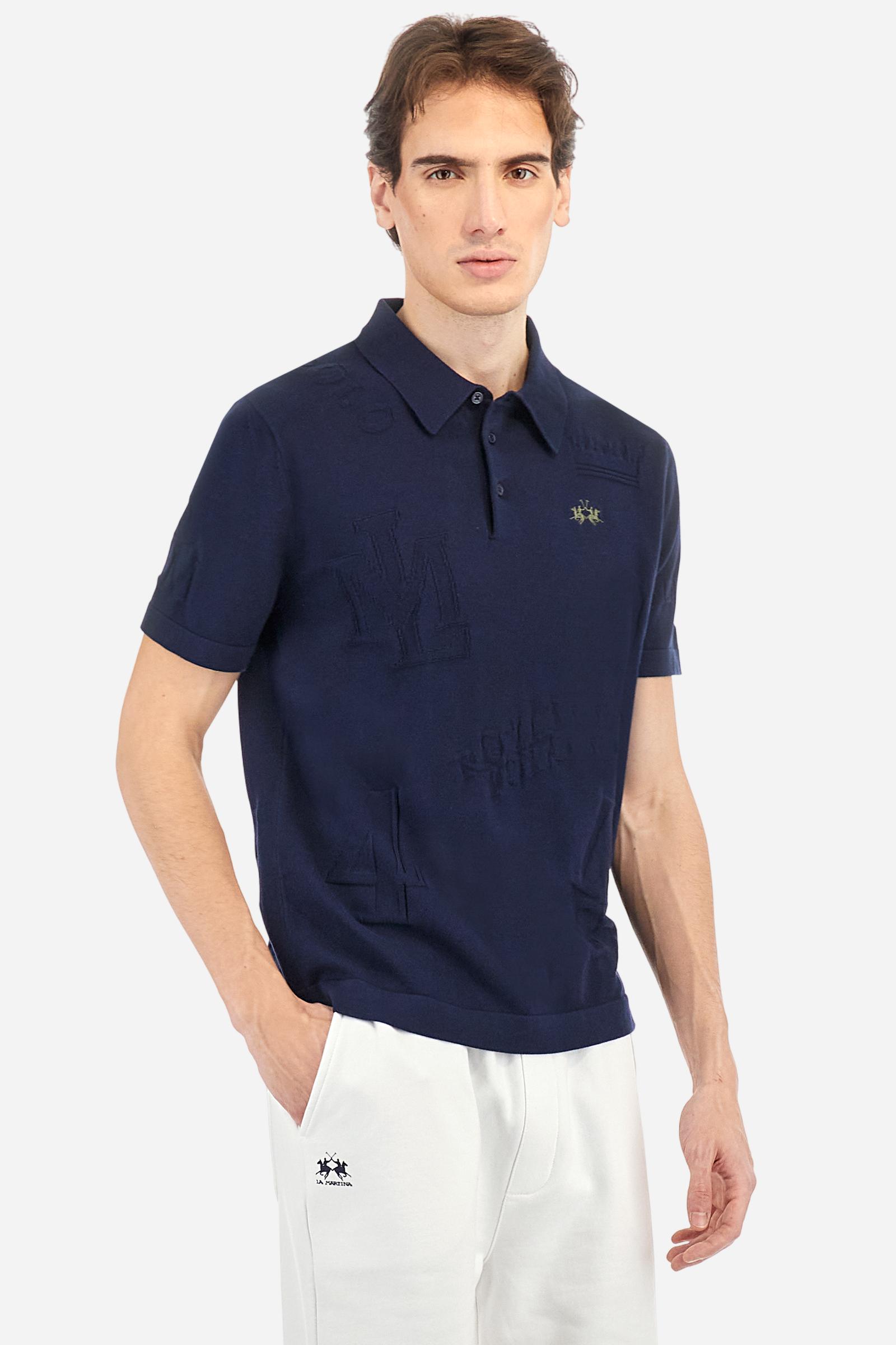 Men's short-sleeved, single-colour knitted polo shirt made of 100% combed cotton yarn. The fastening is with three buttons and the inside of the opening is in vertical rib. Various graphics are present over the garment, made by machine using an inlay technique. The logo on the left side of the chest is embroidered tone on tone. Regular fit. The model is wearing a size L. - Navy