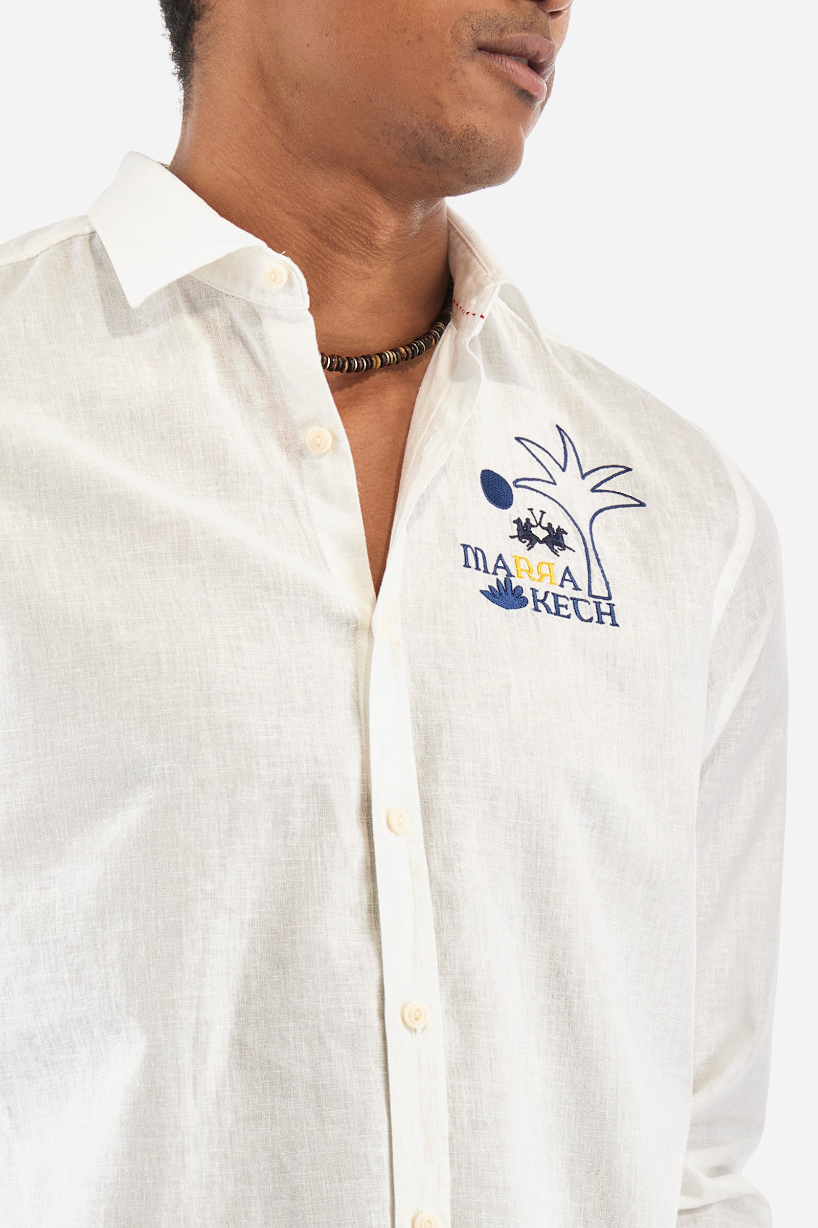 Men's single-colour long-sleeved shirt in cotton and linen. Pointed collar. With buttoned cuffs. A small logo, a palm tree and some lettering are embroidered on the front. The fit is regular. The model wears a size L. - Optic White