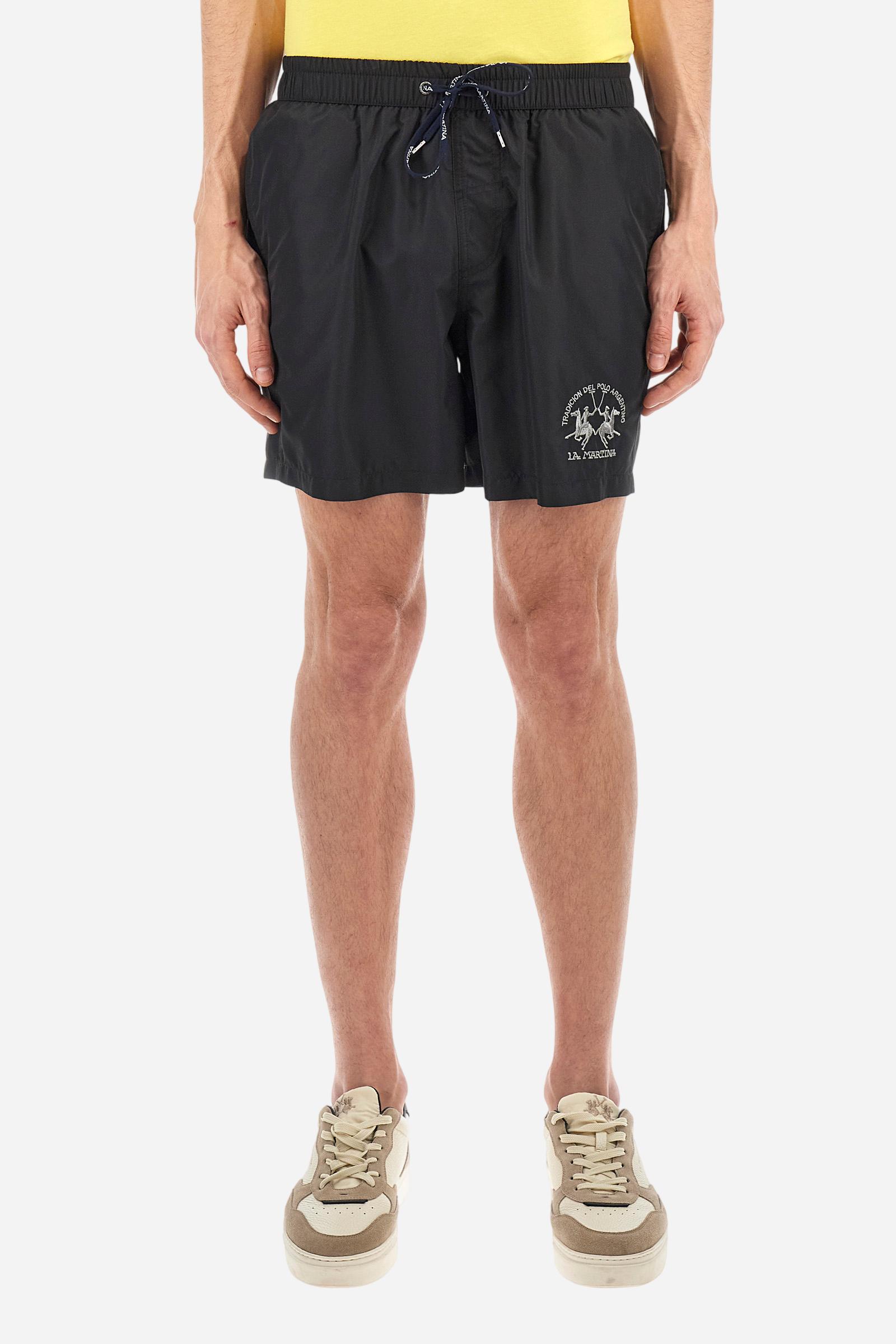 Plain men's swimming shorts made of nylon. Elastic waistband with a personalised drawstring for waist adjustment. On the inside of the shorts is an elasticated mesh brief. Double side pocket on the hips and patch pocket with flap on the back, on the right side only. The large logo is embroidered in a contrasting colour thread on the bottom of the left leg on the front. Regular fit. The model is wearing a size L. - Black