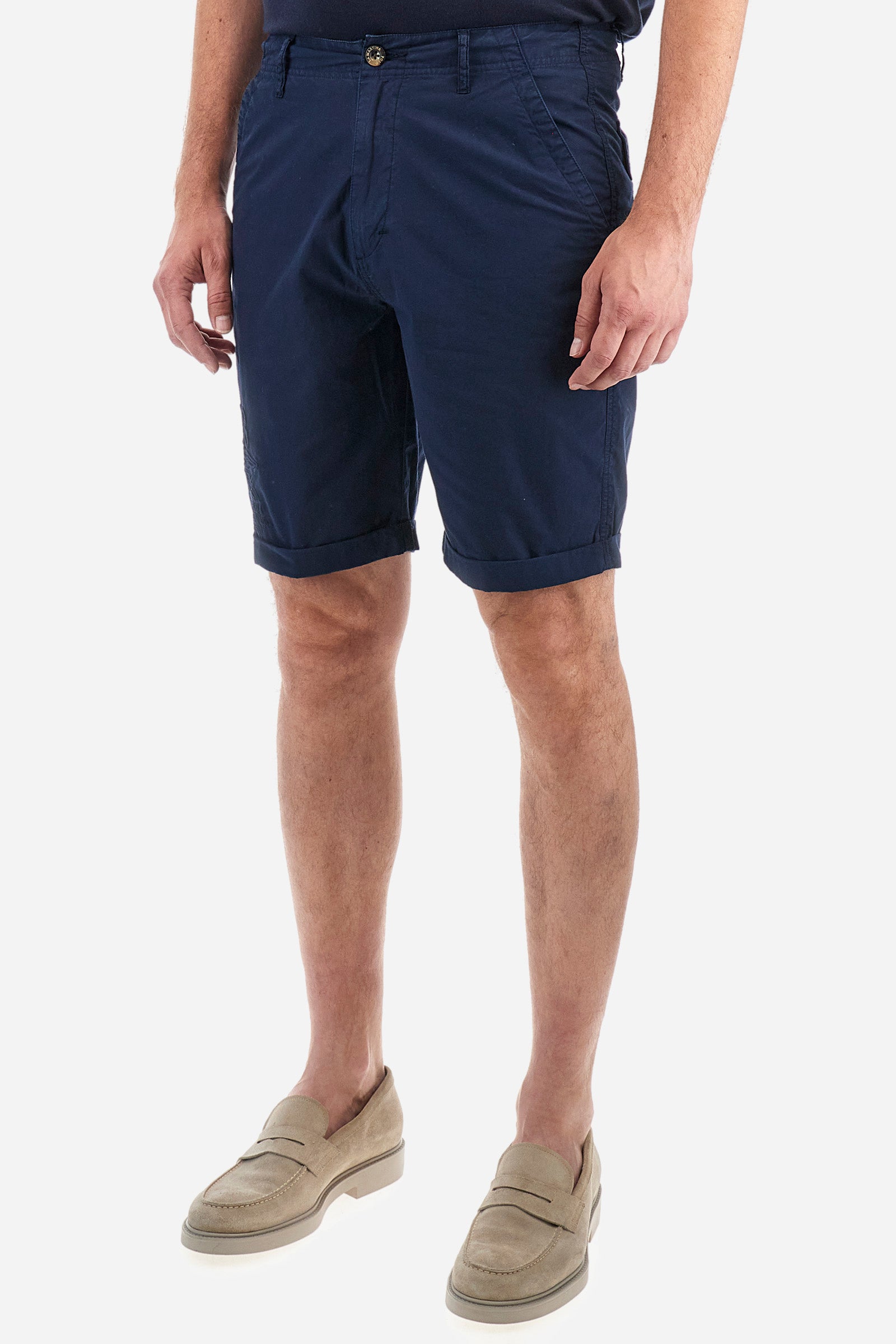 Men's plain Bermuda shorts made from cotton poplin. Fastened with a zip and faux horn button, they feature turn-ups at the hems for a touch of style. The side slant pockets are extremely practical, and the flap patch pockets on the back are fastened with faux horn buttons. Above the right pocket, a woven label explains the brand's quality certification. On the right leg, near the hem, there is an embroidered graphic with numbers and tone-on-tone lettering. Regular fit. The model is wearing a size 33. - Navy