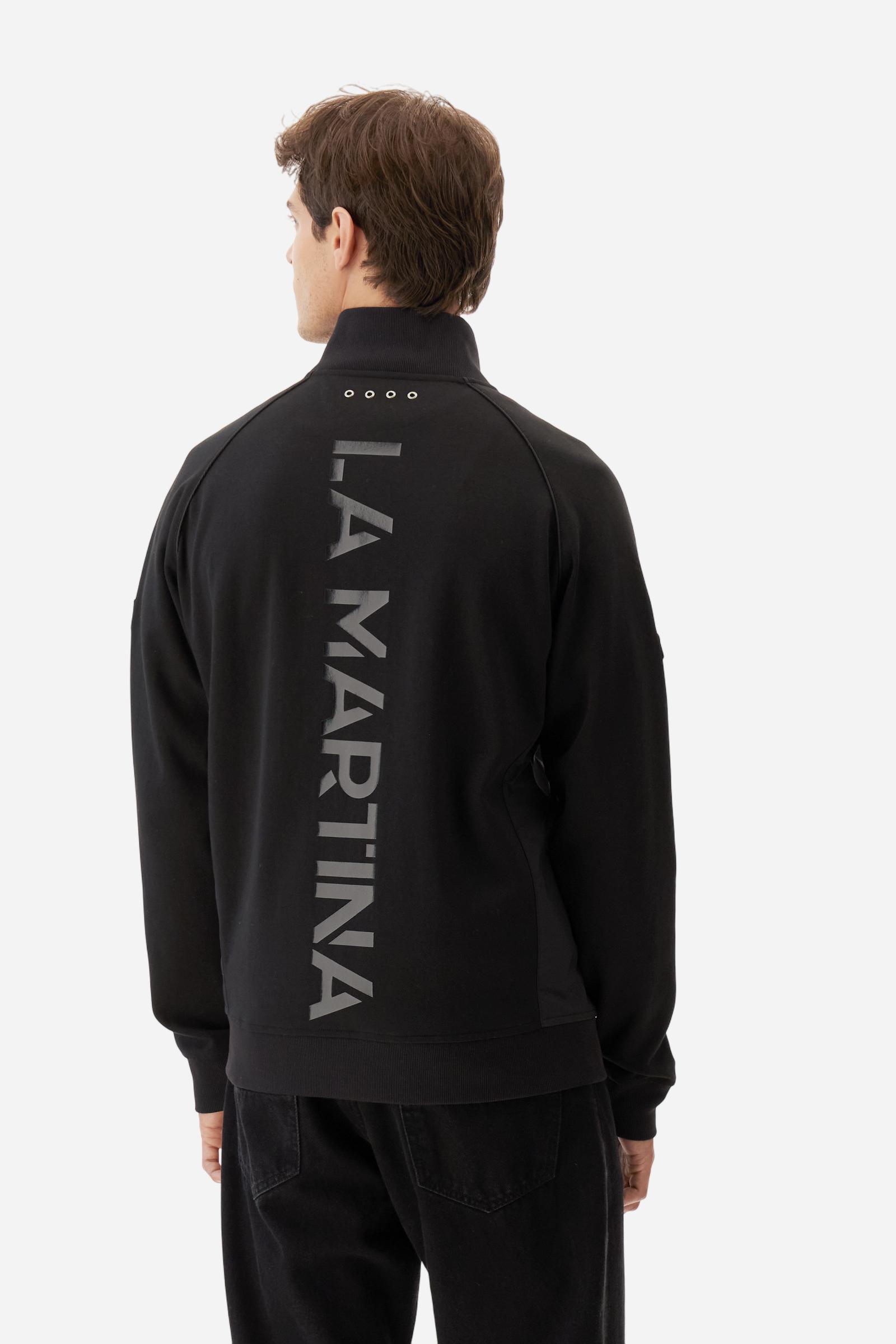 Men's long-sleeved sweatshirt in solid cotton-blend interlock with semi-glossy finish. Features customised front zip, stand-up collar, hem and cuffs in tone-on-tone rib. Large semi-gloss La Martina transfer on the back celebrates the brand's identity, while two patches on the right sleeve recall the Argentine polo association. Regular fit for a practical yet refined style. Model wears size L. - Black