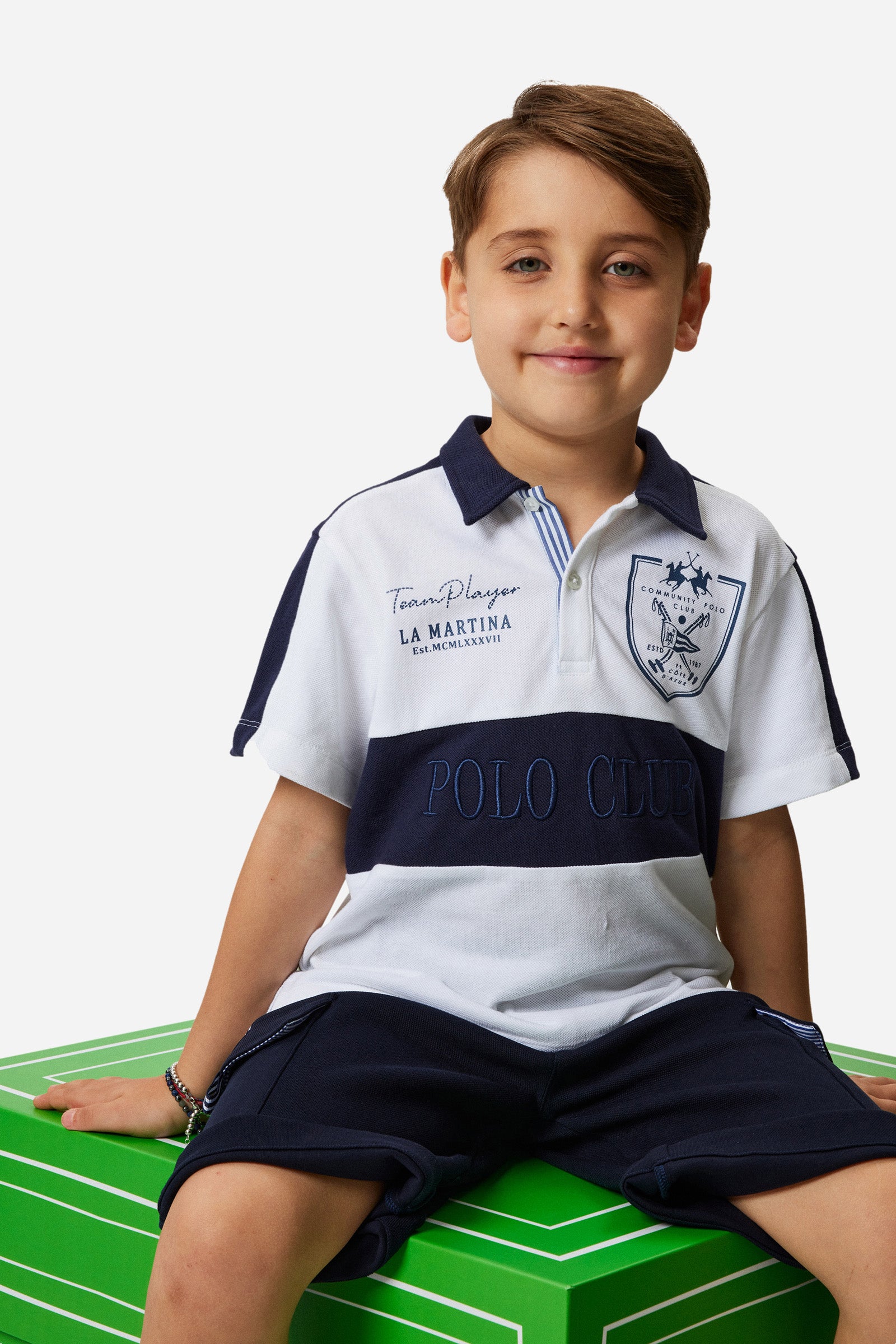 Boys' two-tone polo shirt made of pique cotton. Two-button fastening with contrasting ribbon. There are various embroideries on the garment, both on the front and on the back. Contrasting bands on the central part, on the collar and on the shoulders. Featuring a logo on the front. - Optic White/Blue
