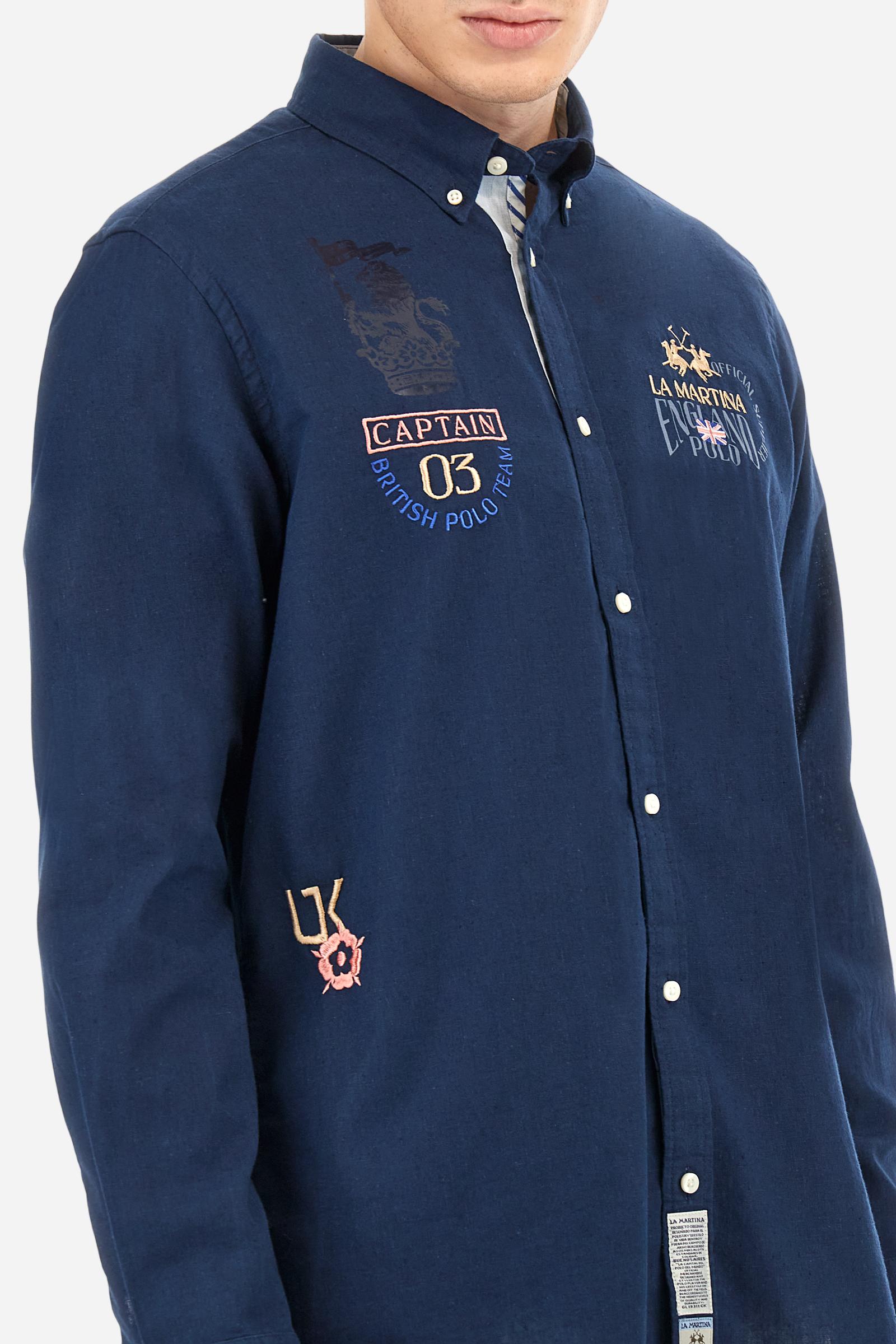 Men's long-sleeved single-colour shirt made of cotton and linen canvas. Button-down collar. Featuring details on the inside of the collar and opening in contrasting colour printed fabrics. The front graphics and logo are embroidered with contrasting colour threads. The fit is regular. The model is wearing a size L. - Navy