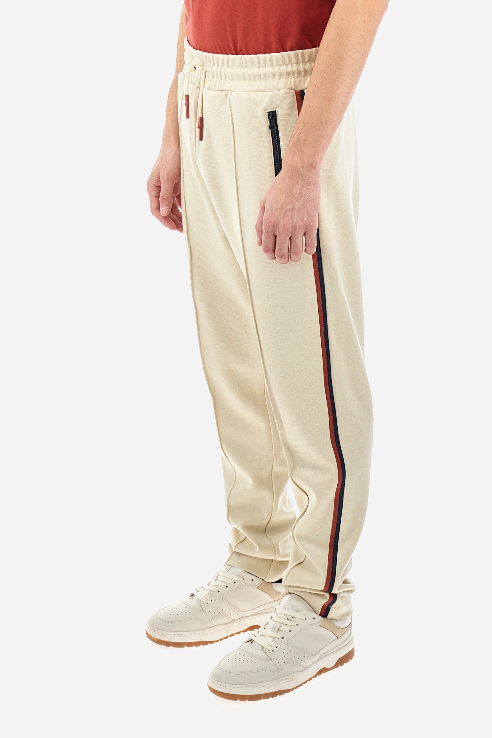 Men's single-colour jogging bottoms in a sweat fabric from the Polo Academy line, with contrasting details. Made of synthetic material. Drawstring waist. Double back pocket with contrasting zip fastening. Another pocket is present on the back. With coloured stripes on the sides of the trousers. The logo is sewn on the back pocket. The fit is regular. The model wears a size L. - Bone White