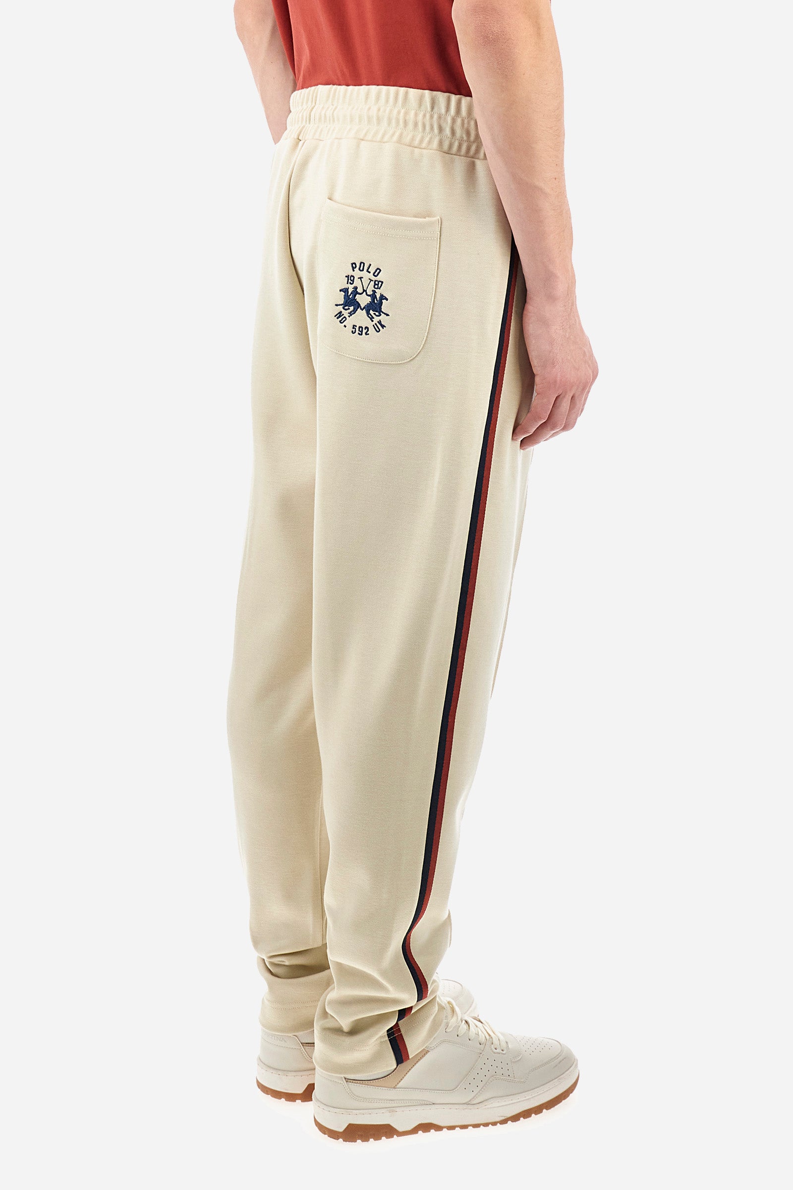 Men's single-colour jogging bottoms in a sweat fabric from the Polo Academy line, with contrasting details. Made of synthetic material. Drawstring waist. Double back pocket with contrasting zip fastening. Another pocket is present on the back. With coloured stripes on the sides of the trousers. The logo is sewn on the back pocket. The fit is regular. The model wears a size L. - Bone White