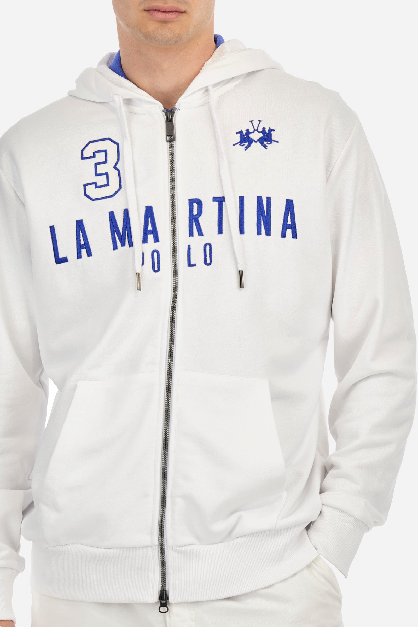 Men's long-sleeved plain sweatshirt made from French terry cotton. Full-zip fastening and hood with adjustable drawstring. On the chest, the La Martina Polo lettering is present as a large, slightly embossed embroidery, while the number 3 is present as a patch made of the same fabric and applied with an embroidered cord in a contrasting colour. The logo is embroidered on the chest, left side. Regular fit. The model is wearing a size L. - OptWhite/Surf TheWeb