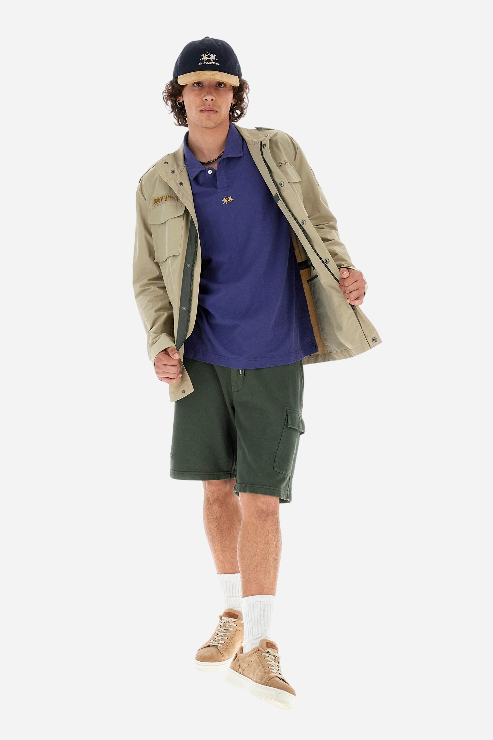 Men's short-sleeved polo shirt in a single colour, made of 100% cotton slub jersey. Fastens with a button. A fabric patch representing the garment's certificate is sewn onto the back. The logo is embroidered in contrast under the opening on the front. Comfort fit. The model is wearing a size L. - Deep Cobalt