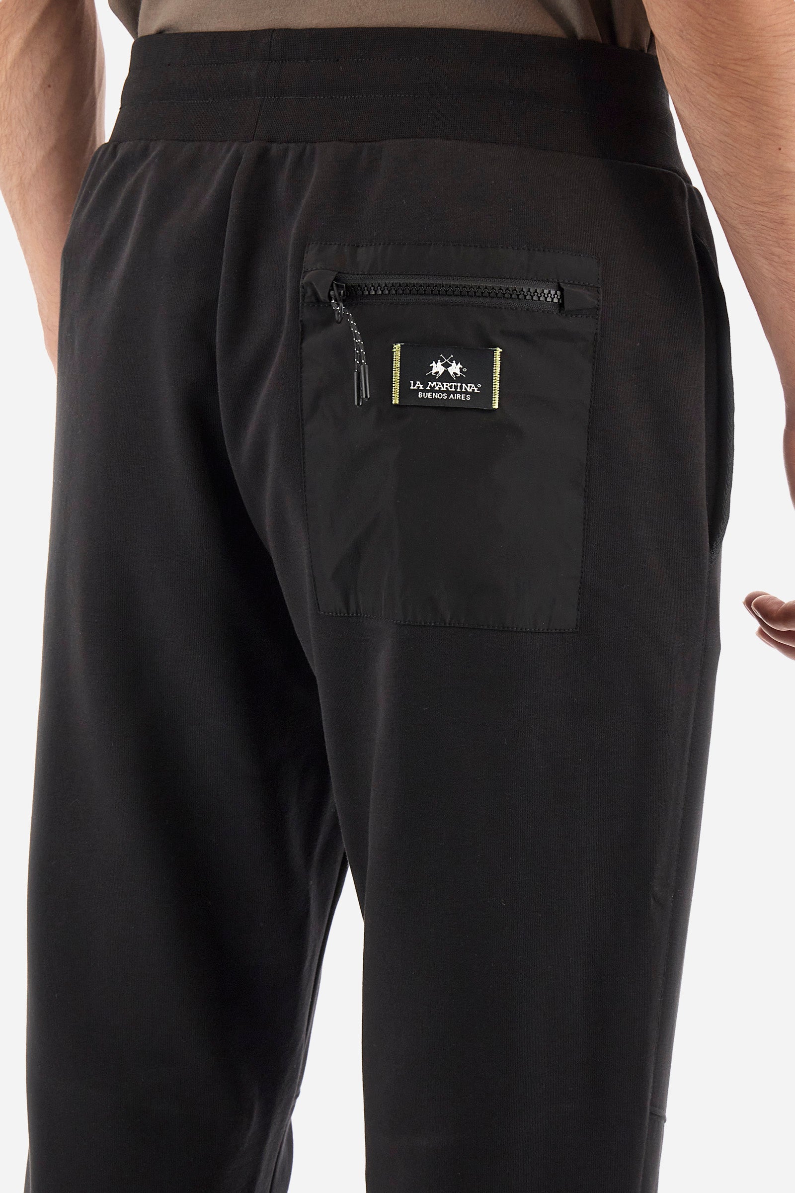 Men's single-colour jogging bottoms in a cotton sweat fabric. With a drawstring waist and double front pocket. With different shades at the bottom of the leg. On the back there is a pocket with a zip fastening featuring contrasting textures and colours. The logo is present on the tag sewn on the back pocket. The fit is regular. The model wears a size L. - Black