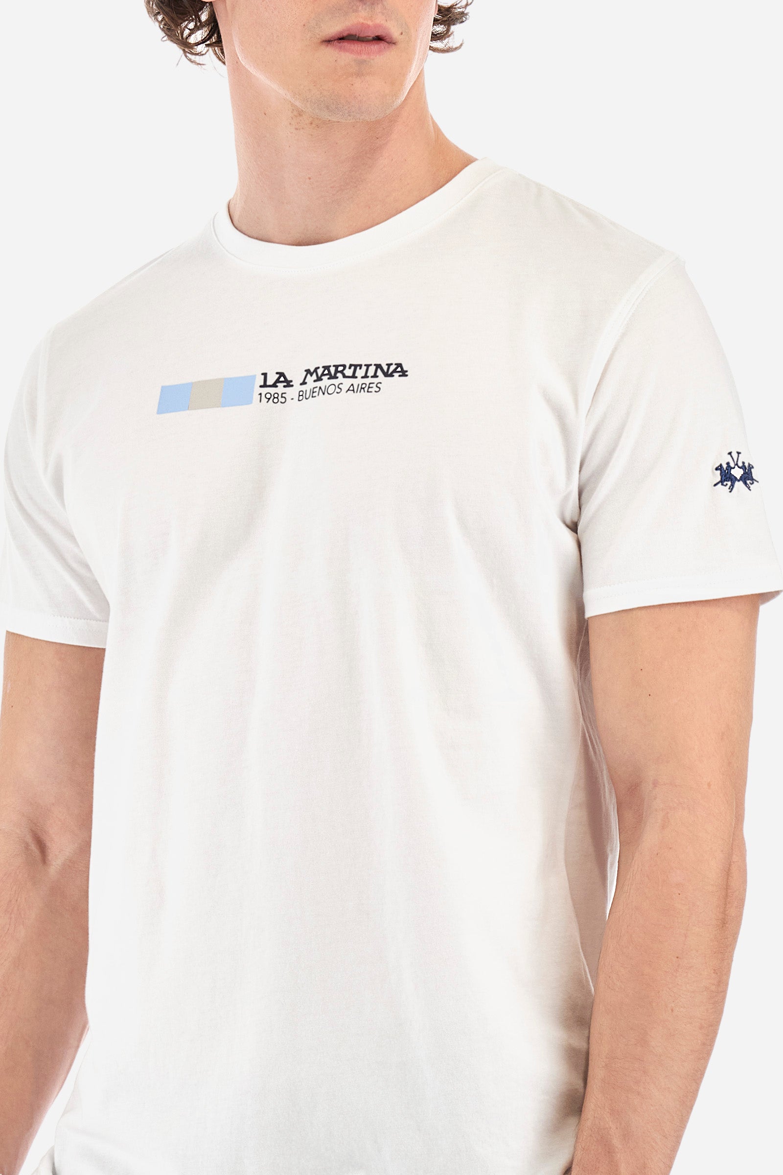 Men's short-sleeved T-shirt with a crew neck in a single colour. Made of 100% cotton. On the front we find the lettering "La Martina 1985- Buenos Aires" with the Argentinian flag. A small logo is embroidered on one of the sleeves. Regular fit. The model wears a size L. - Optic White