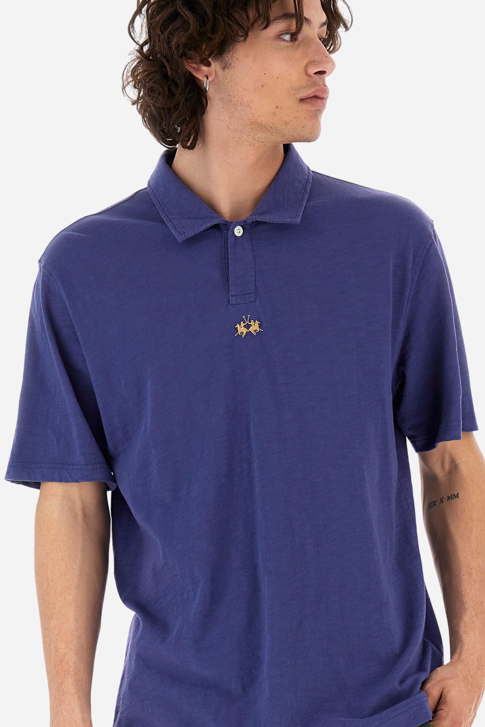 Men's short-sleeved polo shirt in a single colour, made of 100% cotton slub jersey. Fastens with a button. A fabric patch representing the garment's certificate is sewn onto the back. The logo is embroidered in contrast under the opening on the front. Comfort fit. The model is wearing a size L. - Deep Cobalt