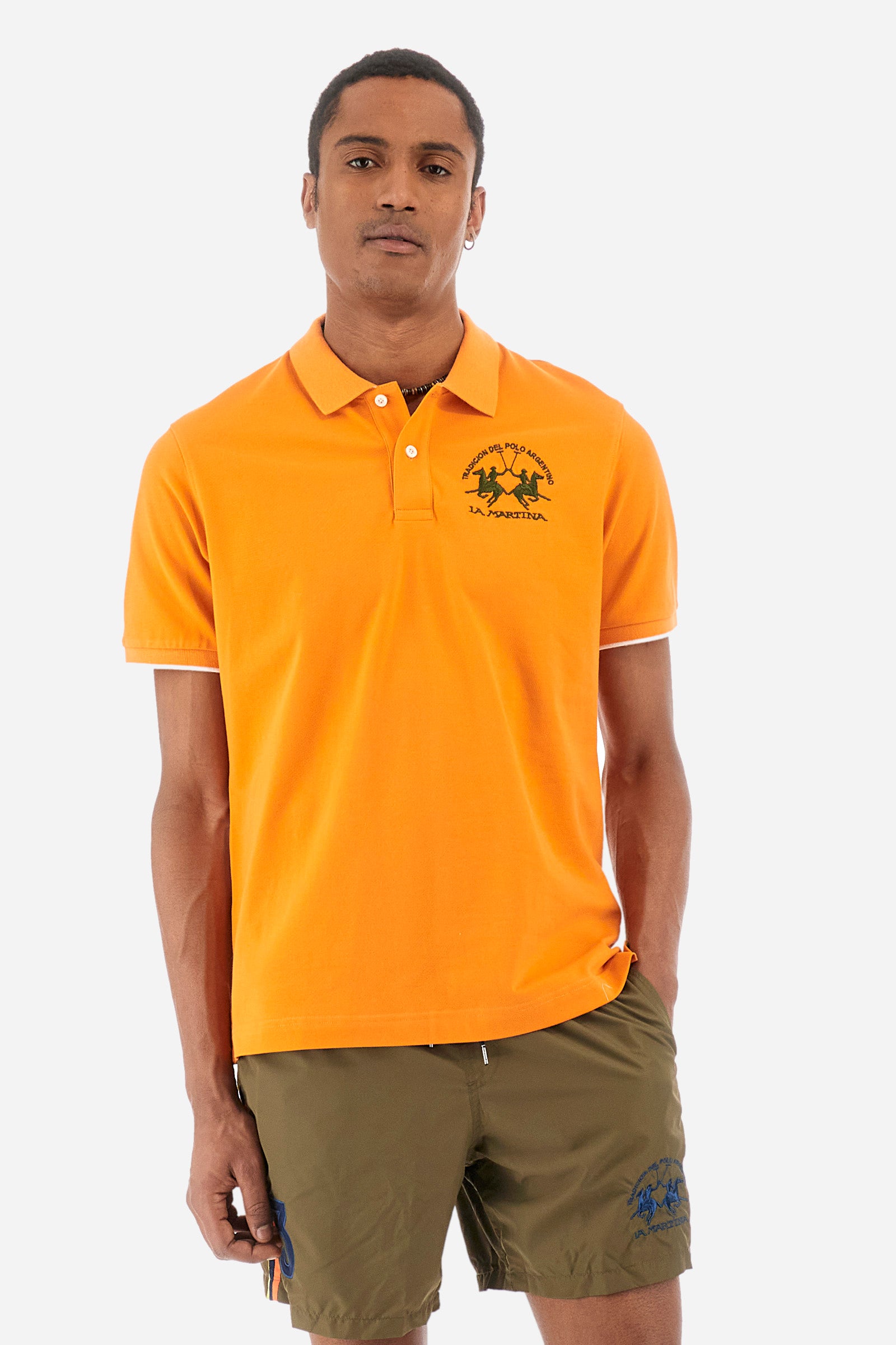 Men’s polo with short sleeves, regular fit. Made of stretch pique cotton. Classic model, with large embroidered logo in contrasting tone on the chest and profiled sleeve edges. The collar is accompanied by the writing La Martina, in contrasting tone. Ideal if worn with a denim collection. The model wears a size L. - Celosia Orange