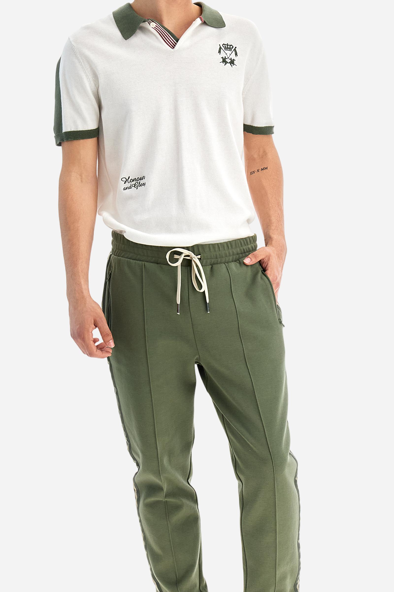 Single-colour men's jogging trousers made of lightweight cotton-blend interlock fleece. Drawstring waistband. Side pockets with matching zip fastening. On both sides, there are multicoloured striped jersey bands. The front features vertical ribbed detailing. The logo is embroidered in colour-contrasting thread on the back, under the strap, towards the right side. Regular fit. The model is wearing a size L. - Thyme