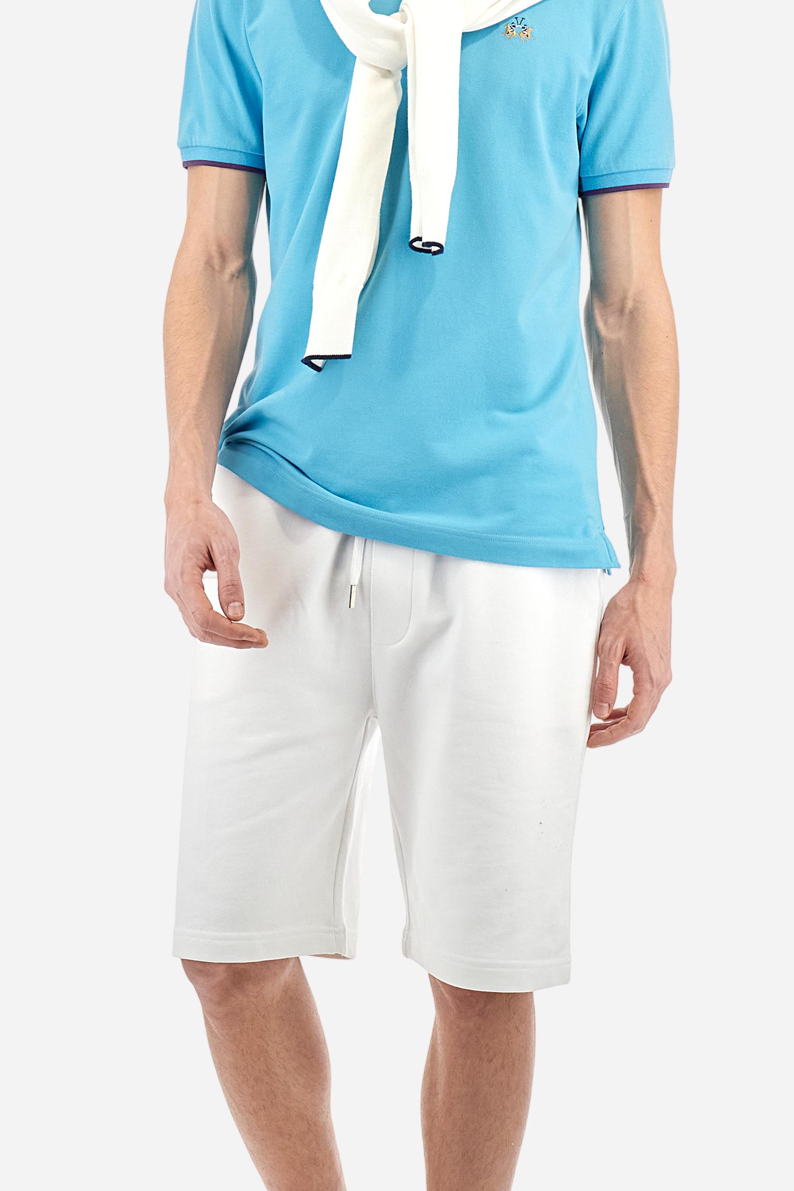 Short-sleeved, single-colour men's polo shirt made of stretch cotton piqué. Fastens with two buttons. The collar and cuffs are ribbed, and there is a colour-contrasting trim at the bottom of the collar. Inside the collar there is a grosgrain ribbon of a different shade. The logo is embroidered on the chest in a contrasting colour. The fit is slim. The model is wearing a size L. - Blue Mist