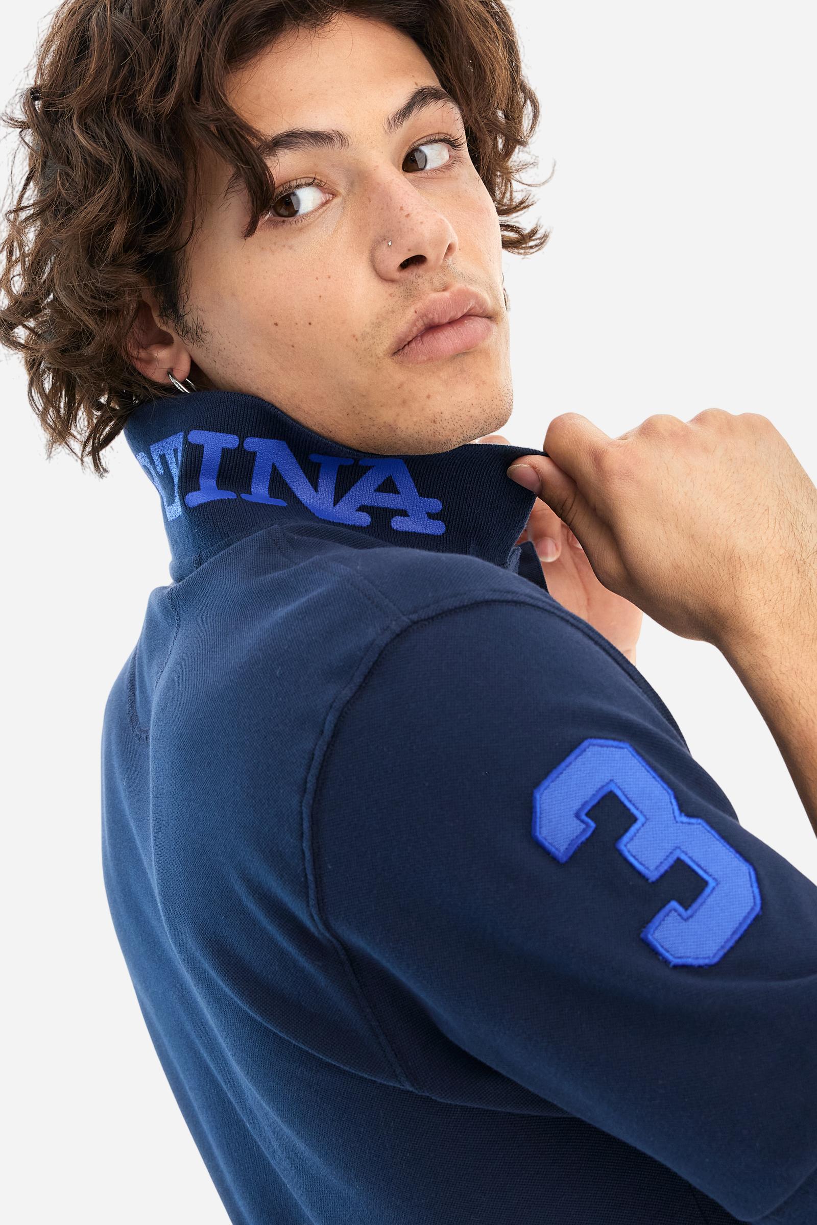 Men's plain short-sleeved polo shirt made from stretch piqué. Two-button fastening. The collar and cuffs are made from tone-on-tone ribbed fabric. A contrasting fabric patch depicting the number 3 is appliquéd on the right sleeve. The logo is embroidered on the left side of the chest in contrasting thread. Under the collar, there is a large contrasting print of the La Martina lettering. Regular fit. The model is wearing a size L. - Navy